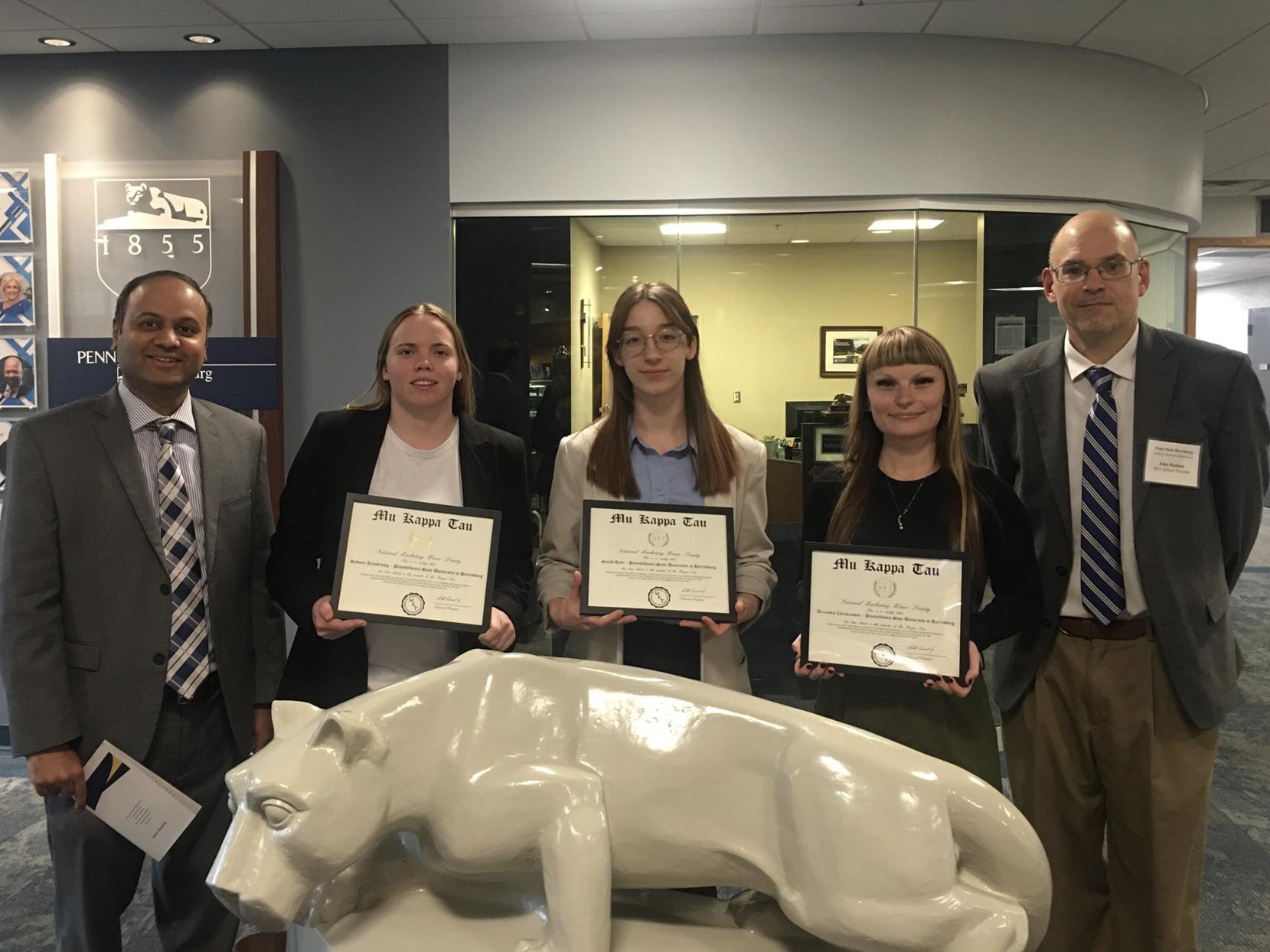 A group of people stand around the Nittany Lion statue in Olmsted Building. Three students hold certificates.