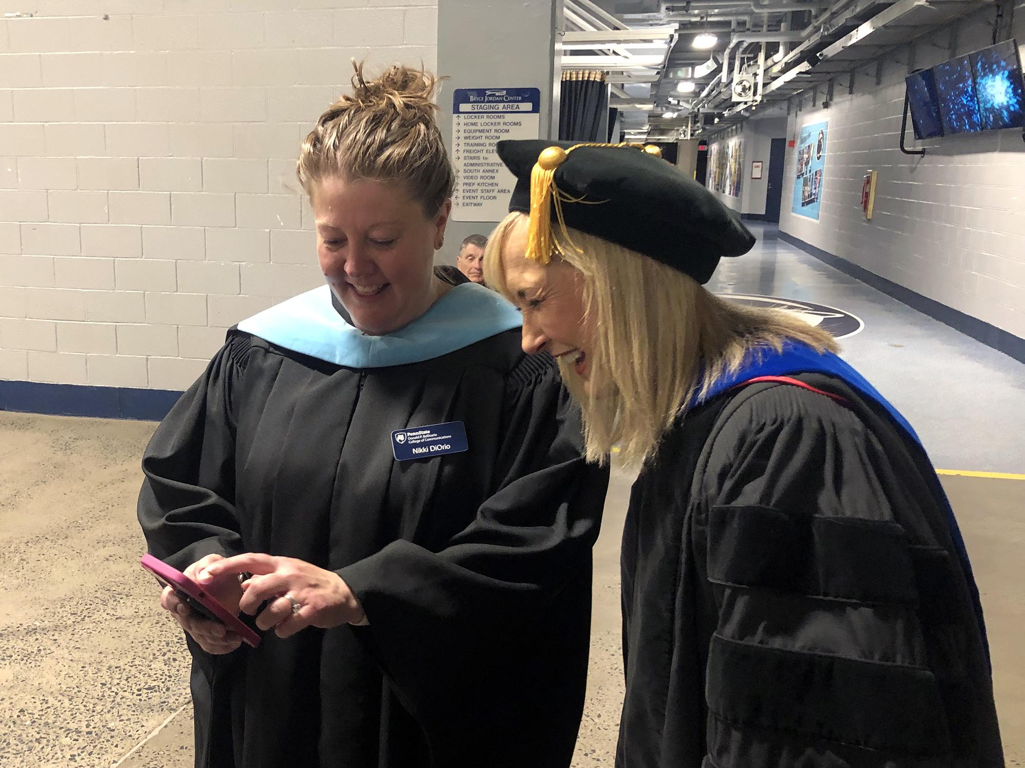 Two women lean over a phone together and laugh