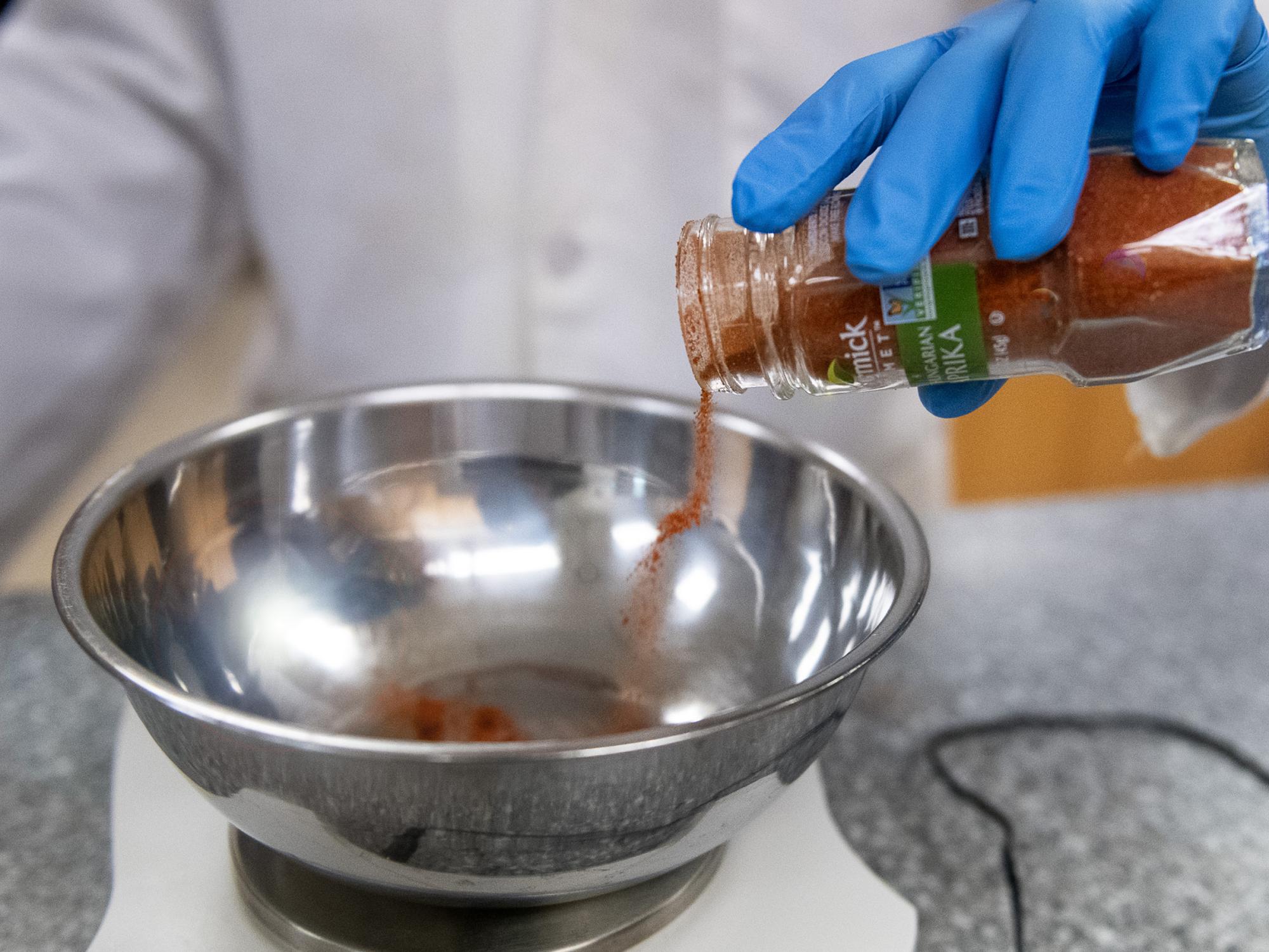 A gloved hand pouring spice into a bowl