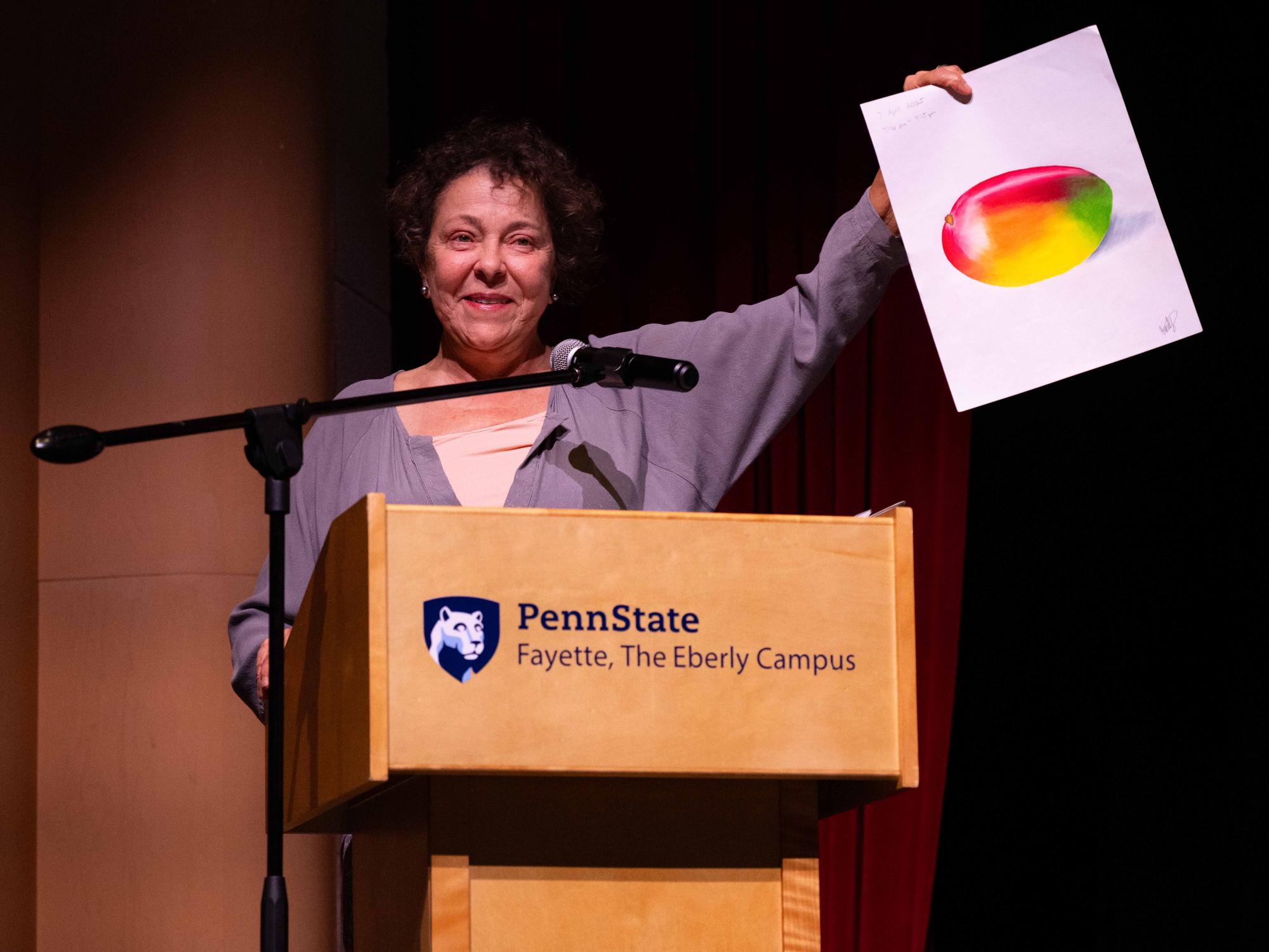 A presenter holds up Emily Kimmel’s award-winning drawing on stage during the Student Awards Banquet, where Kimmel received the Jerome Joseph Guzy Memorial Award in Art.