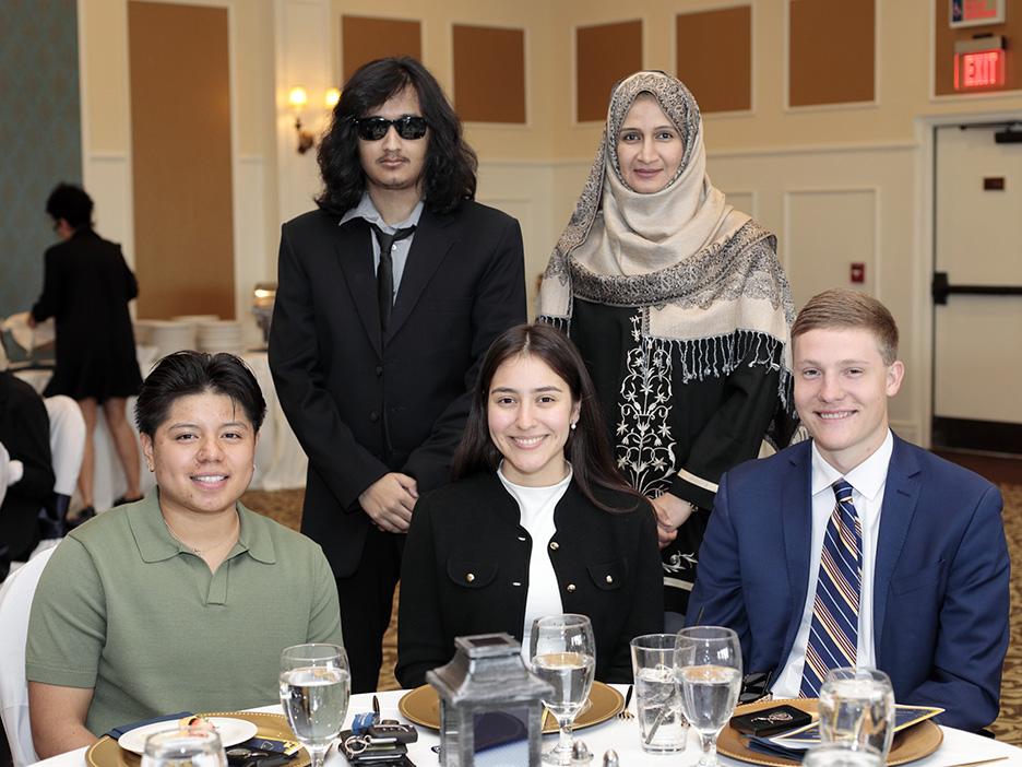 Three people seated at a table with two people standing behind them.