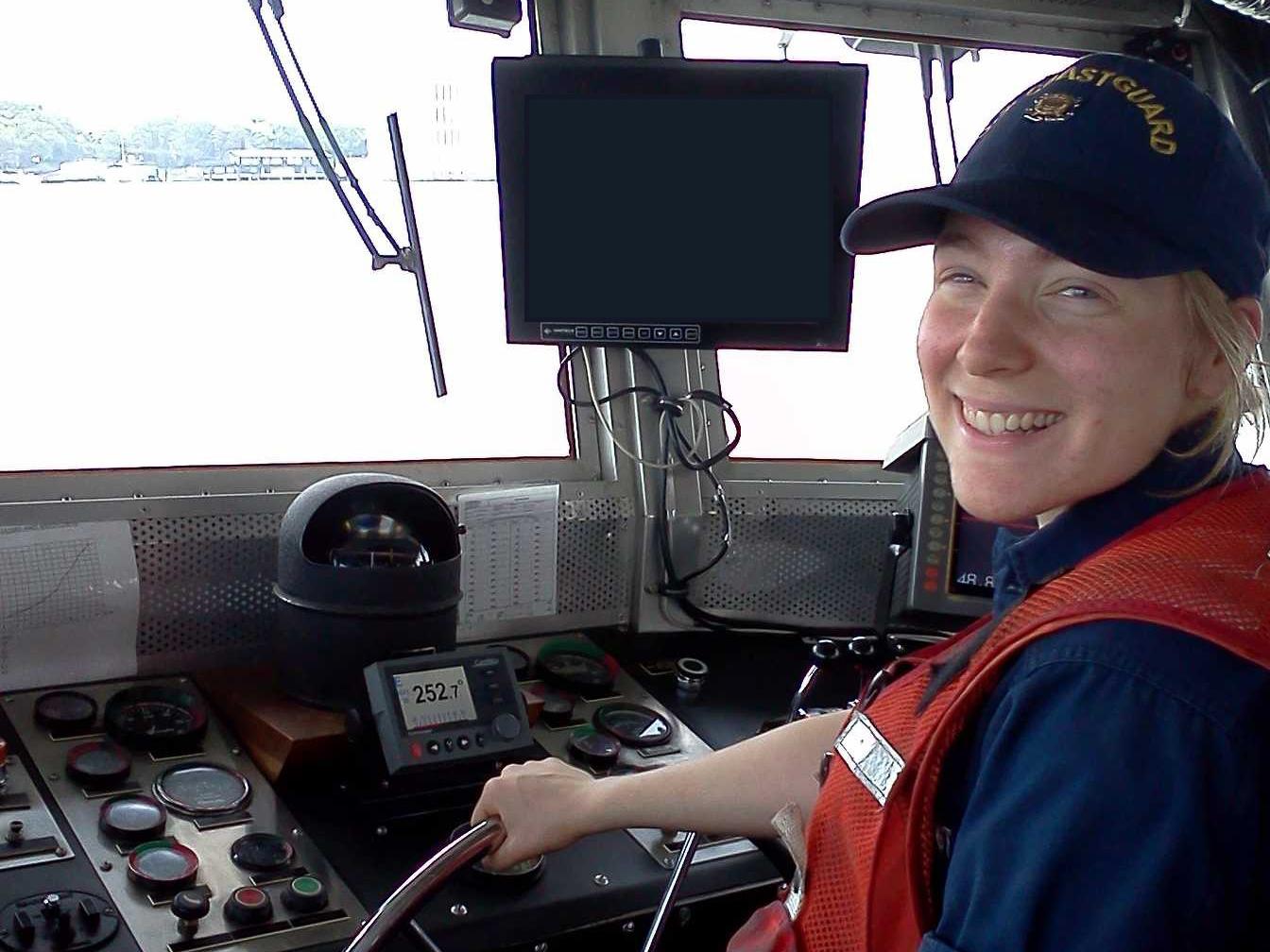 Jessie Wolfen wears a Coast Guard uniform and holds the steering wheel of a boat.
