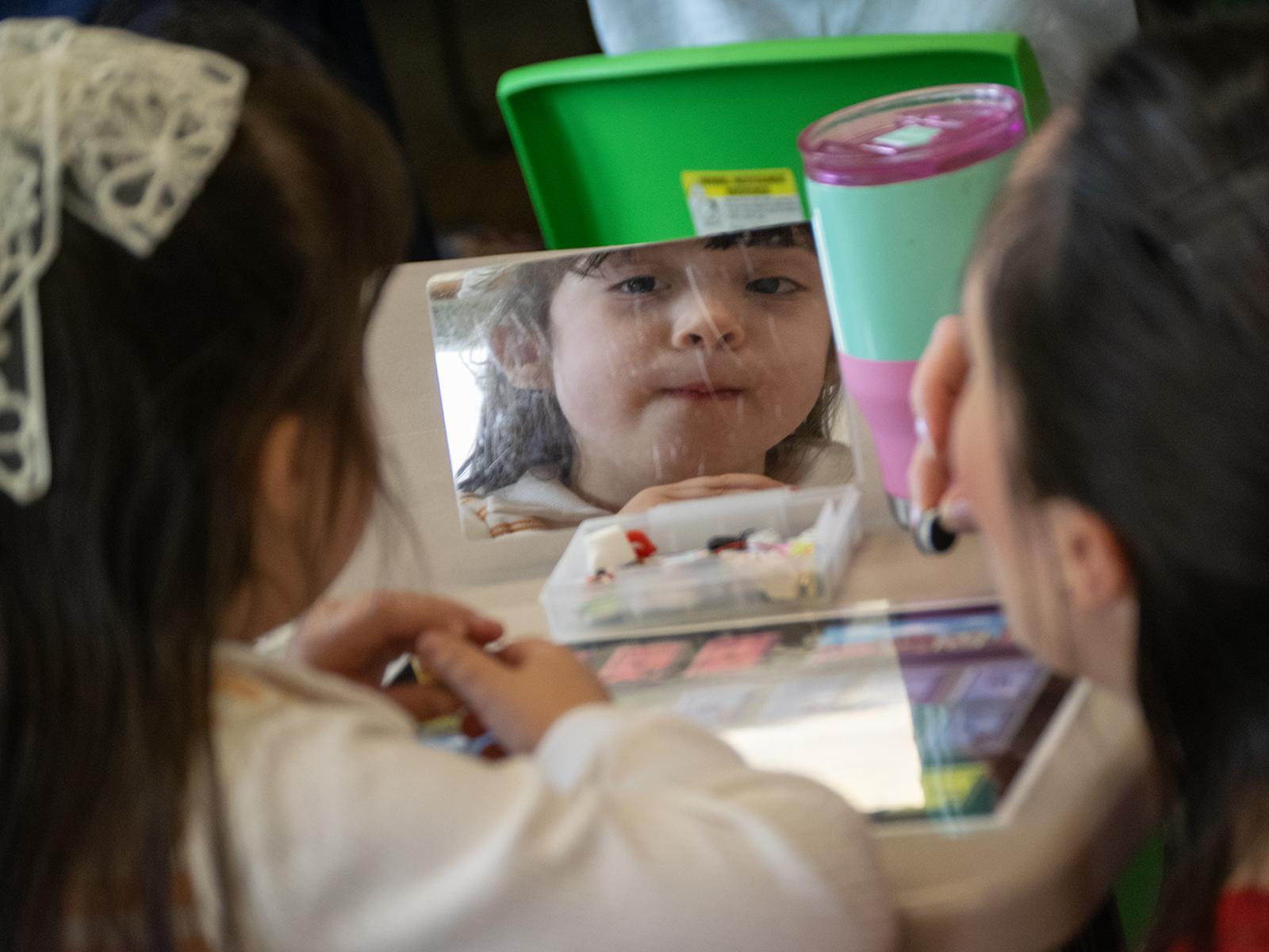 a child looks into a small mirror, lips pursed together