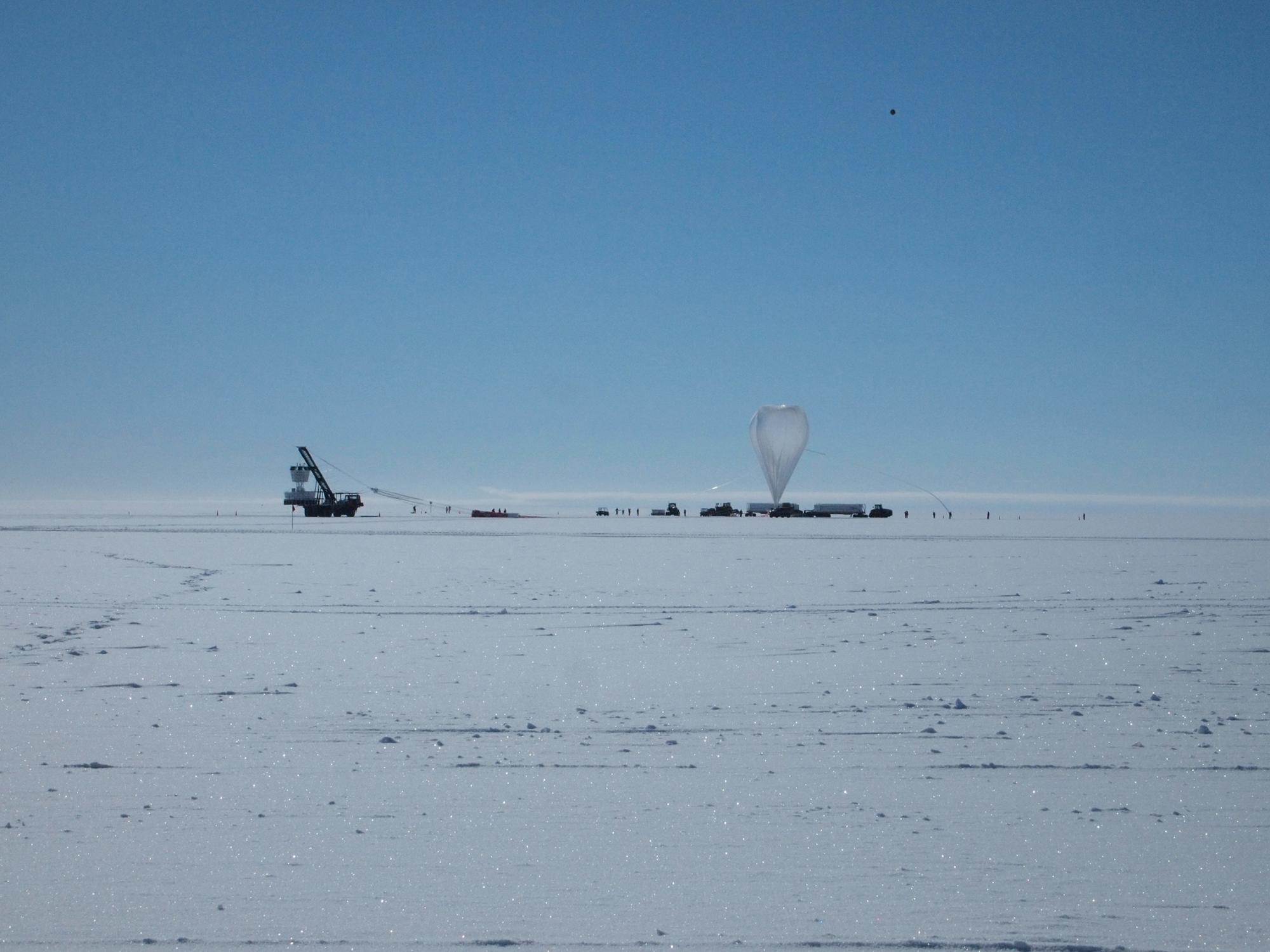 Una fila de vehículos, instrumentos detectores y un globo gigante sobre el hielo.