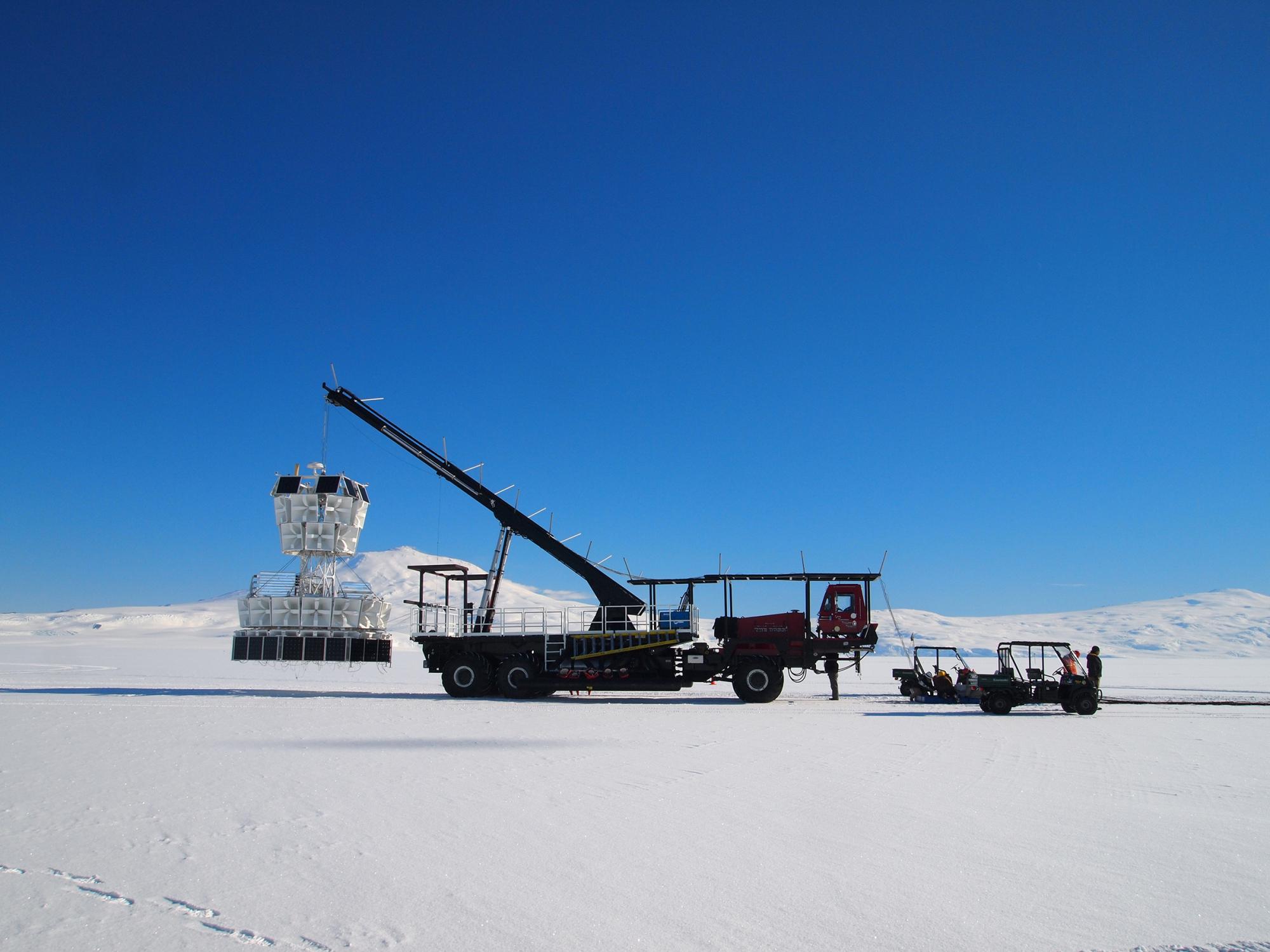 A crane with a giant detector instrument drives on the ice