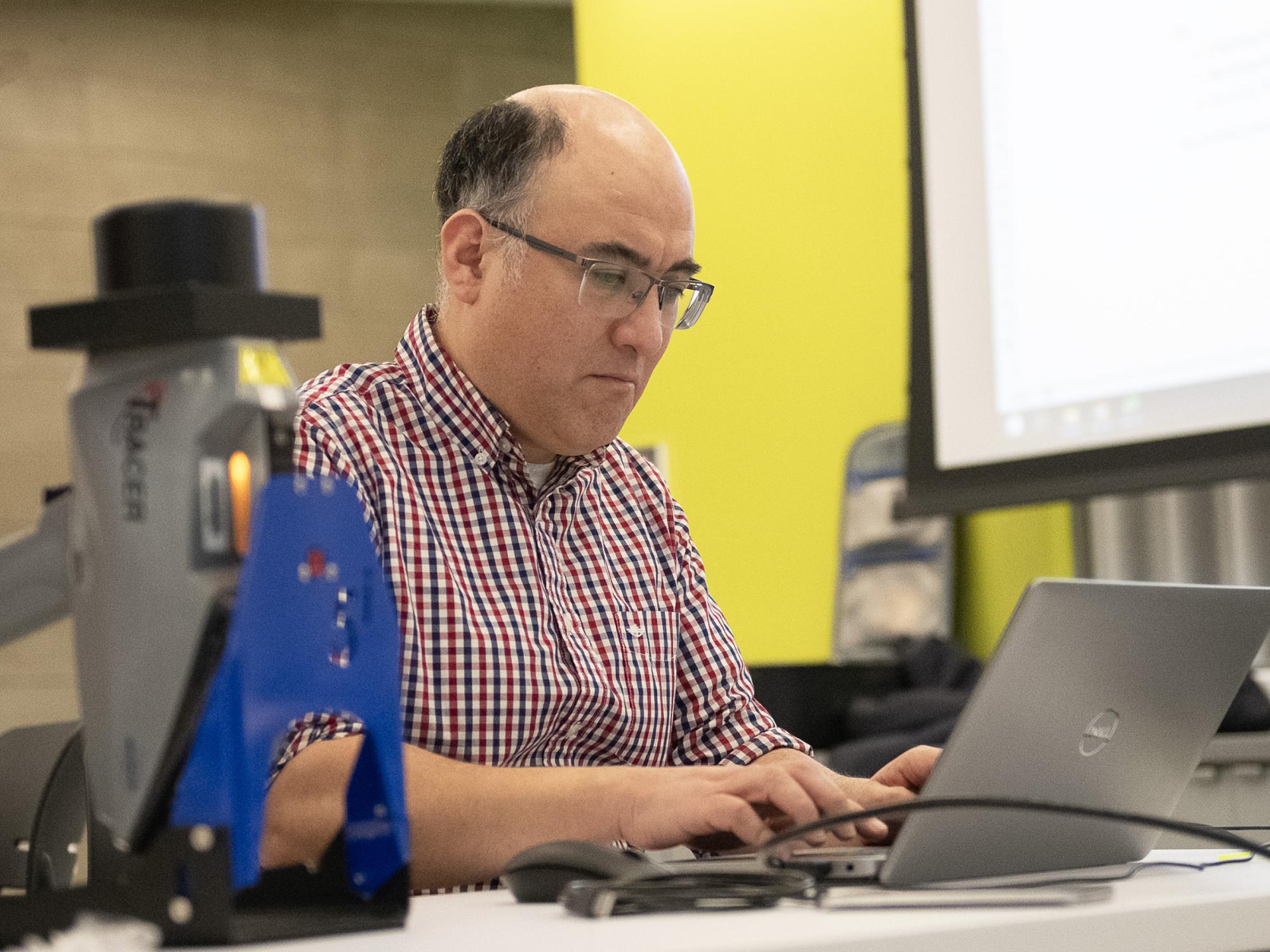 A researcher working next to a microscope and a computer