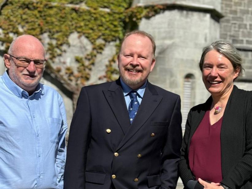 Two men and a woman standing outside, smiling