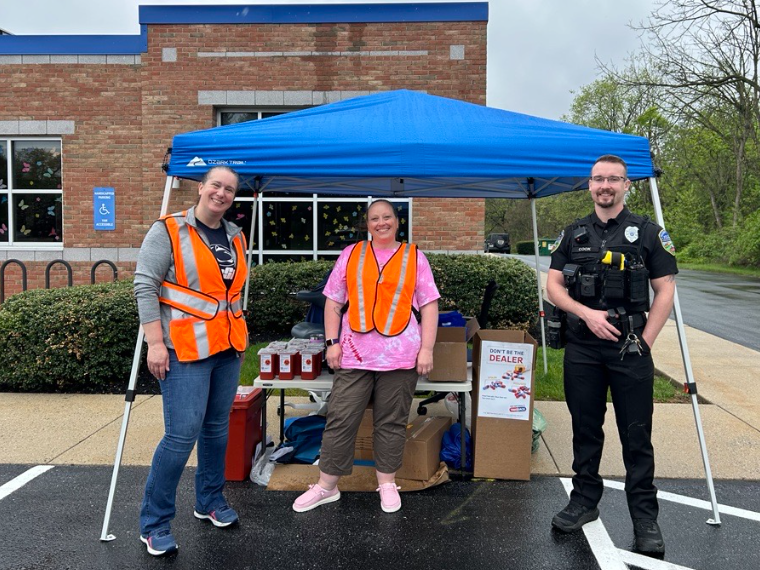 Two colleagues and a police officer stand with collection boxes and sharps containers outside a medical practice.