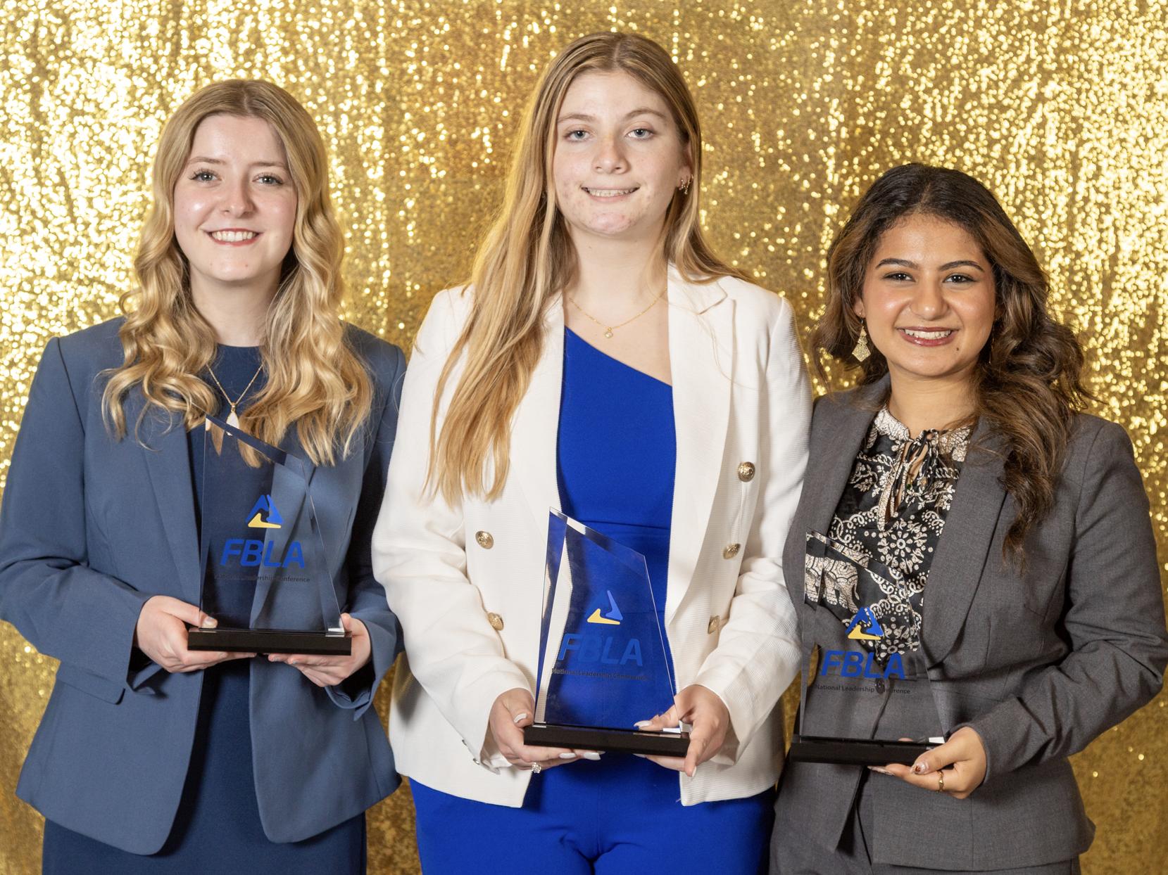 Three women hold FBLA trophies