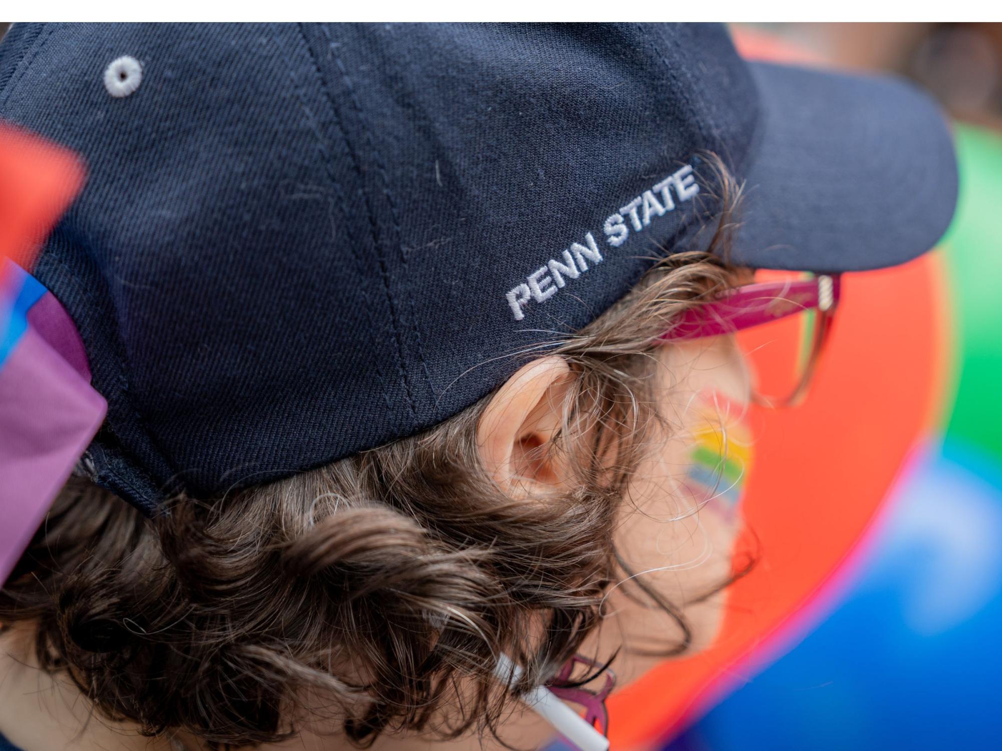 person with dark curly hair wears penn state ball cap