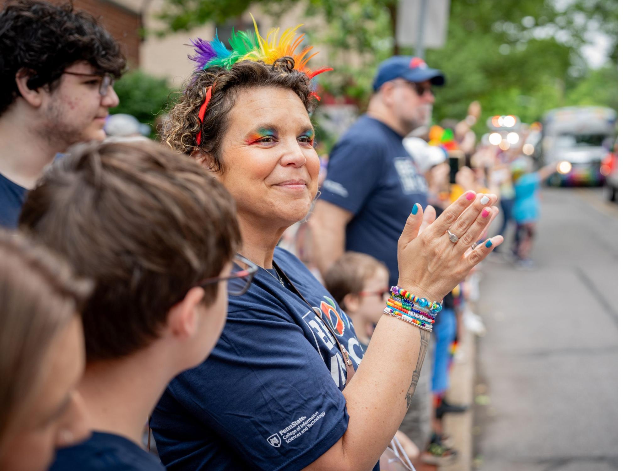 person with rainbow headband and eyeshadow applauds passing parade
