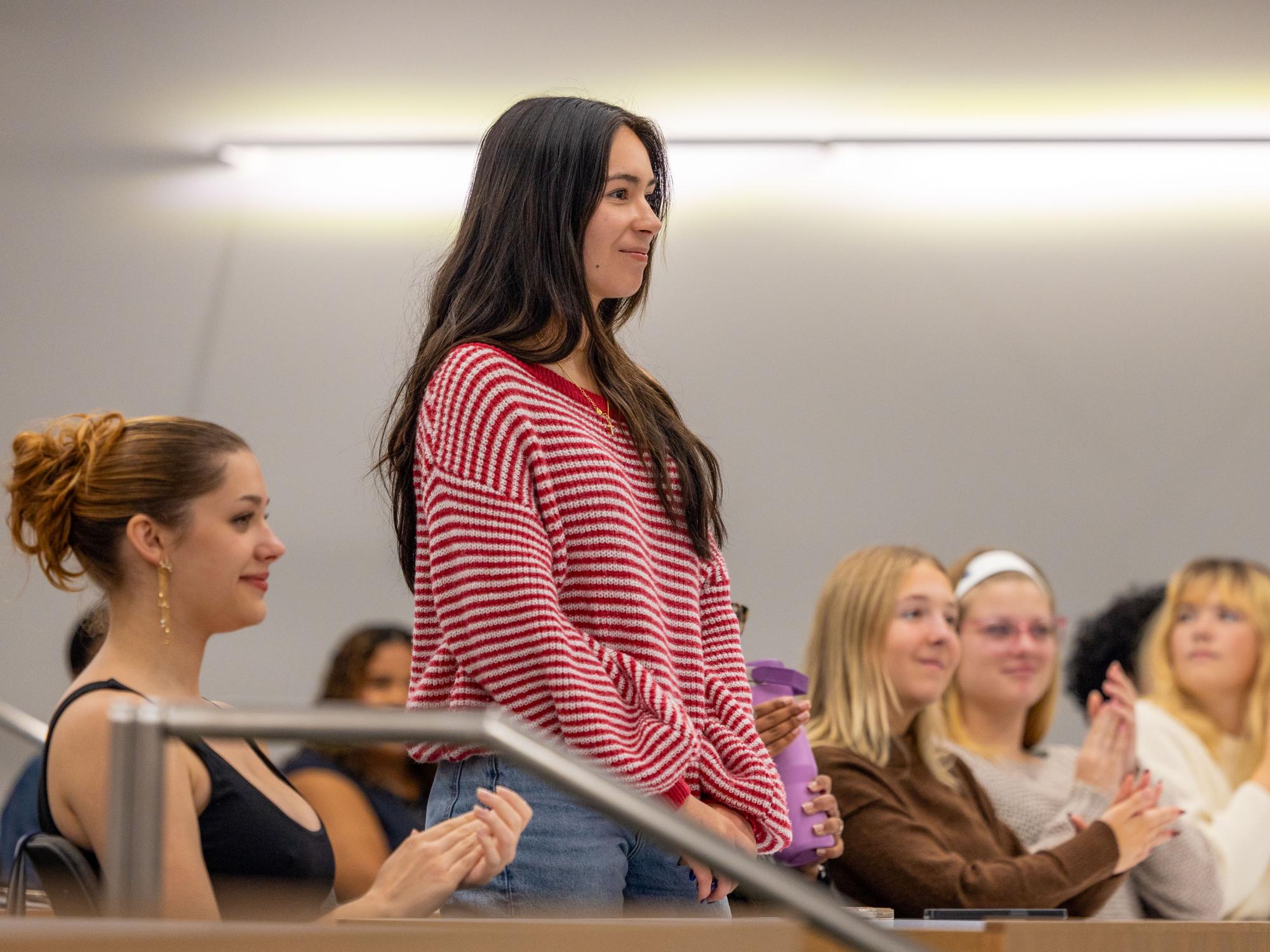 Diana Lopez stands up, as sitting students applaud.
