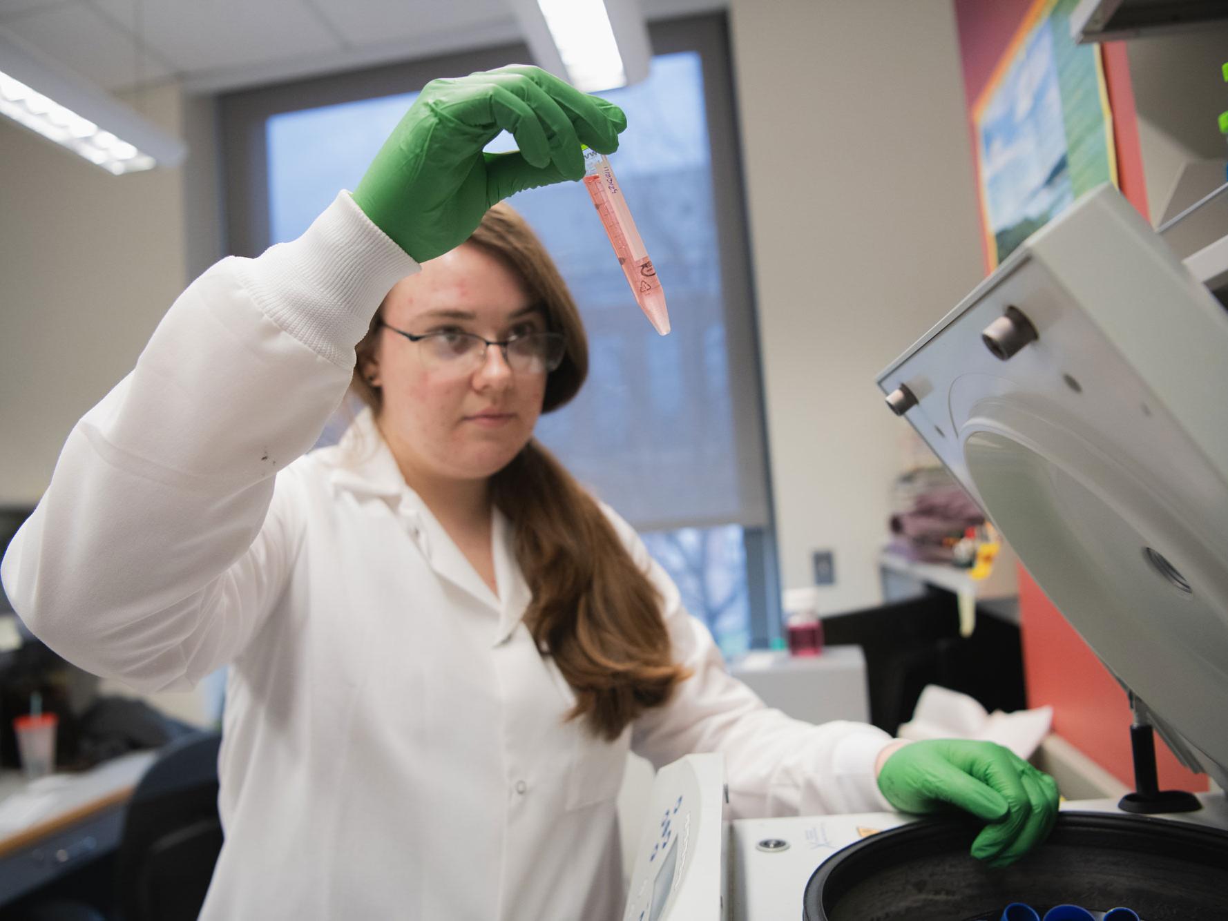 Serena Noss, wearing gloves, holds up tube of liquid in the lab