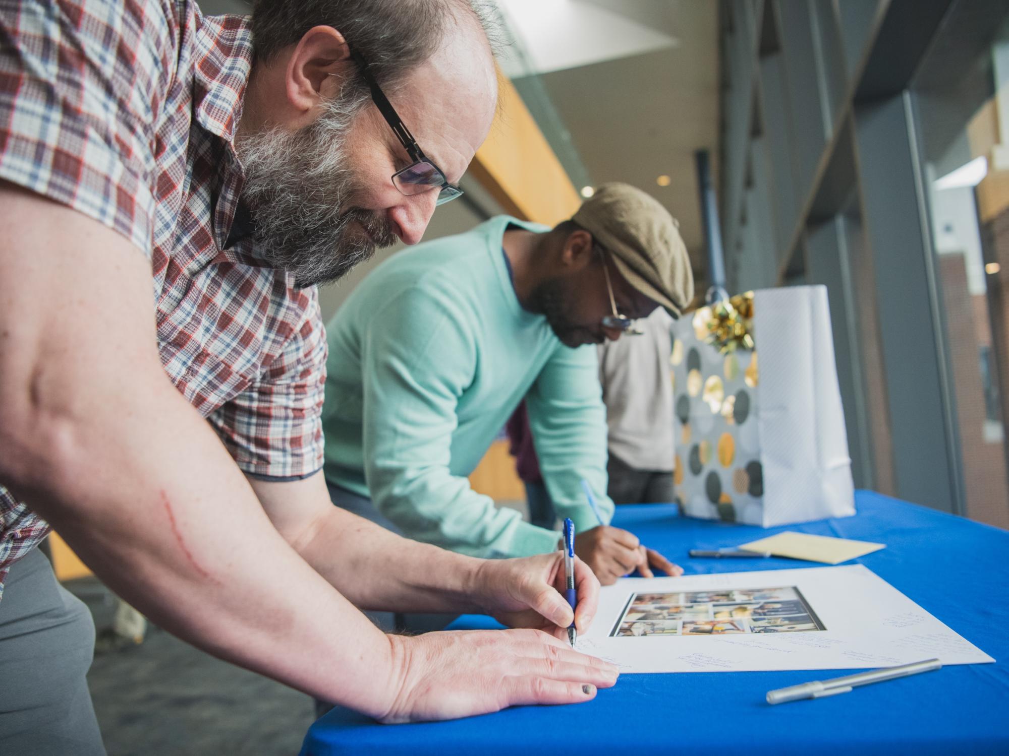 Two people signing a photo for Jackie Bortiatynski at her retirement party.
