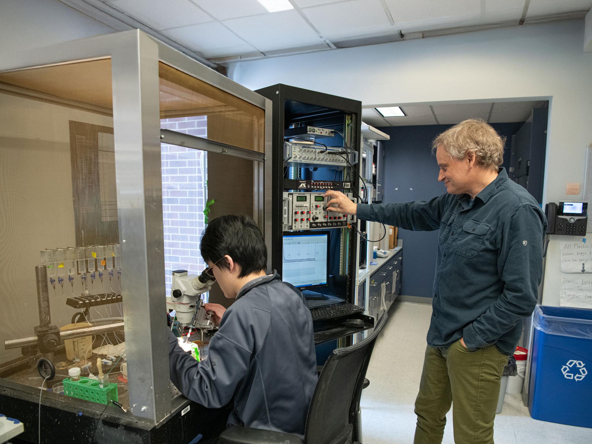 Zhaoyang Jiang works at microscope while Tim Jegla looks on