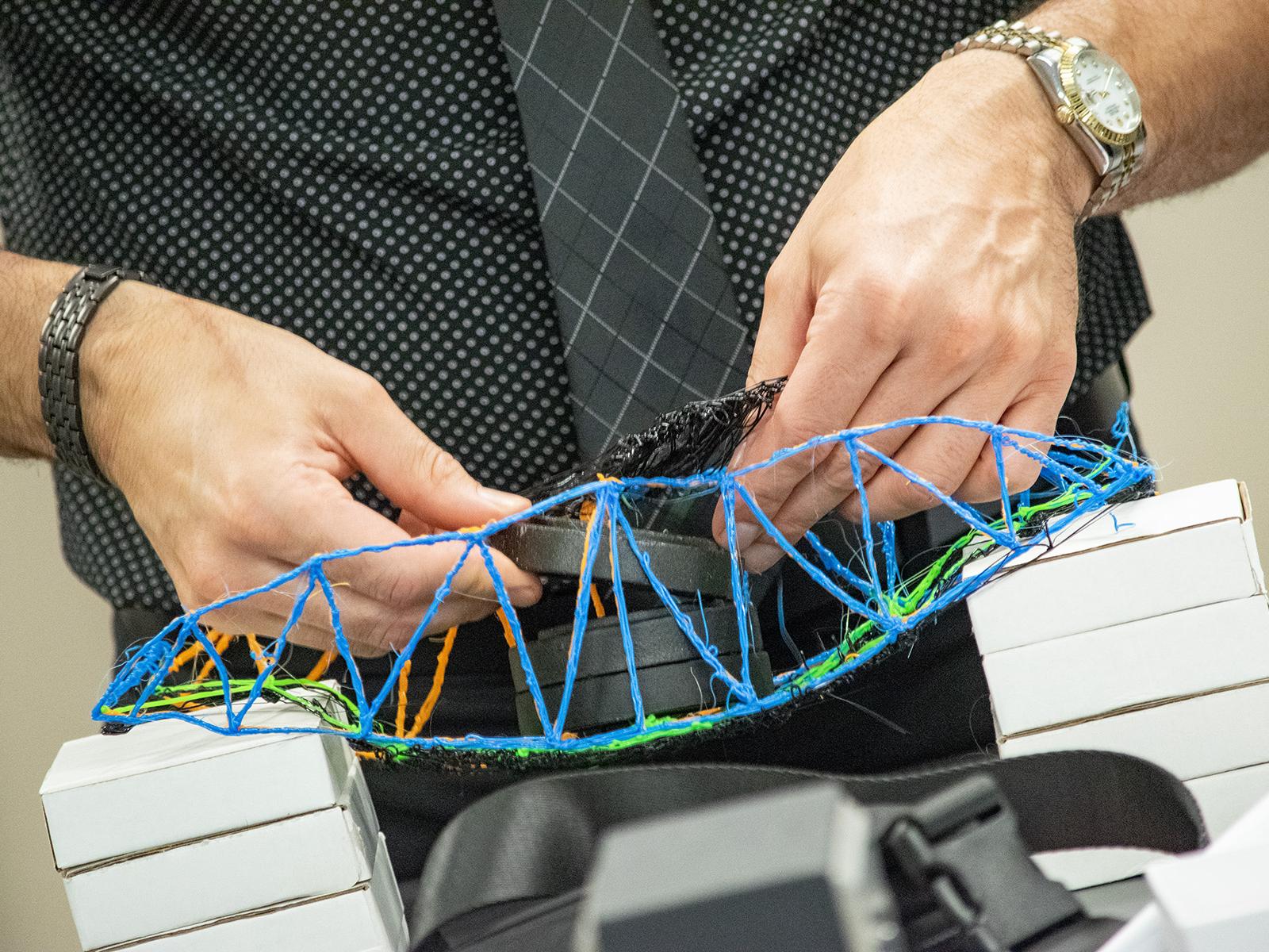 Closeup of hands placing weights onto a 3D printed bridge