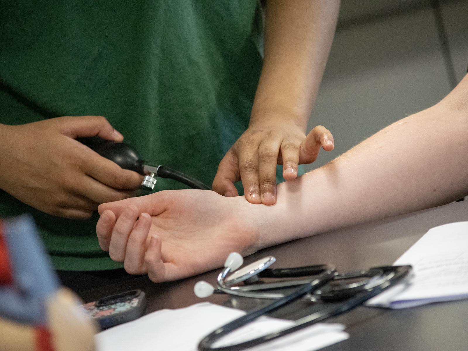 Closeup of a student checking another's pulse while taking blood pressure readings