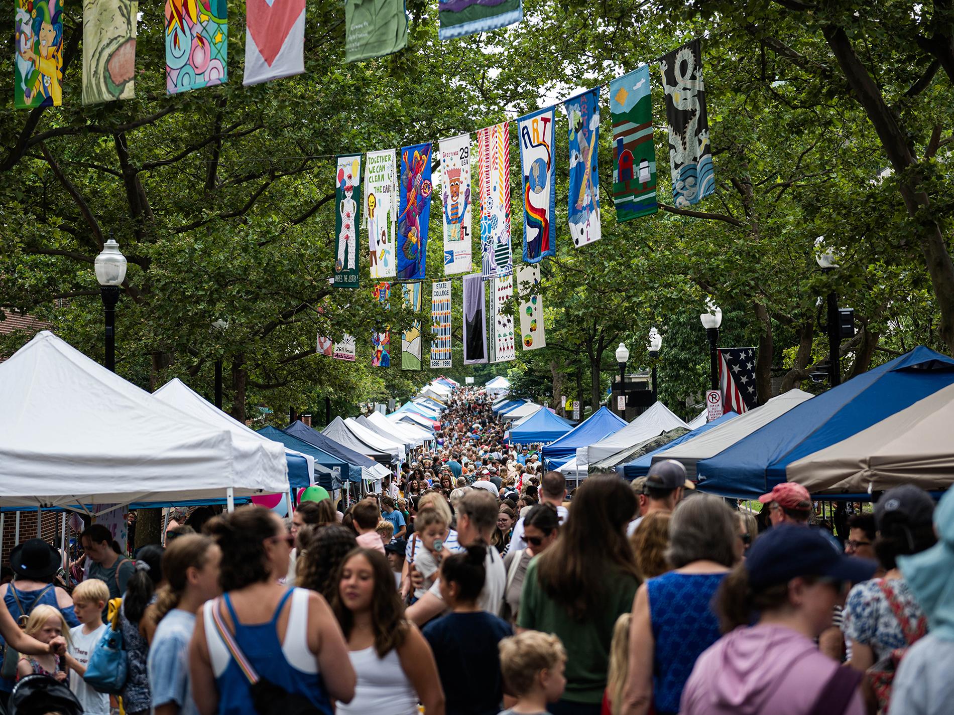 A crowd of people wander through tents set up in a row on each side of the street