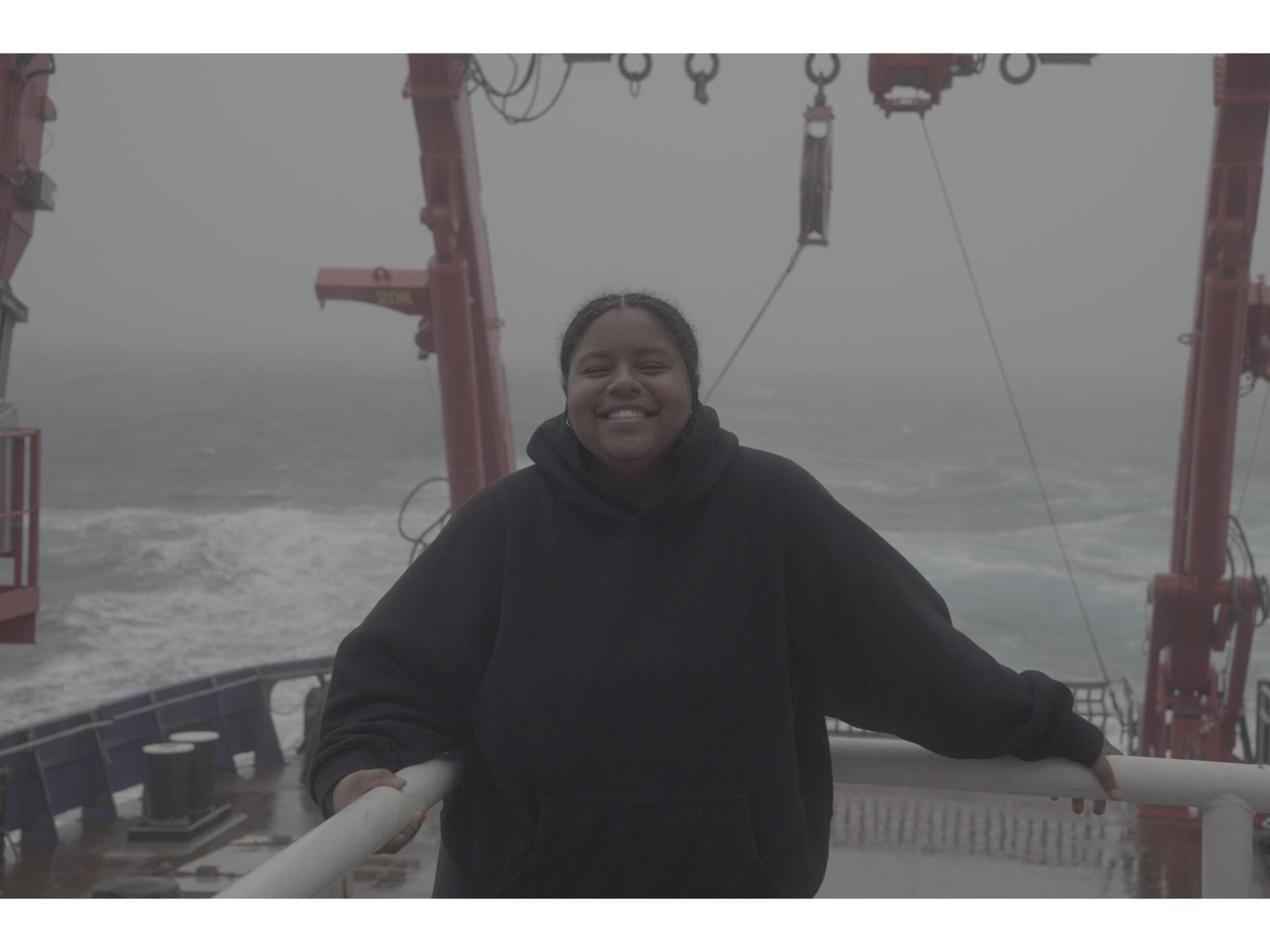 smiling person wearing black hoodie on ship sailing foggy sea