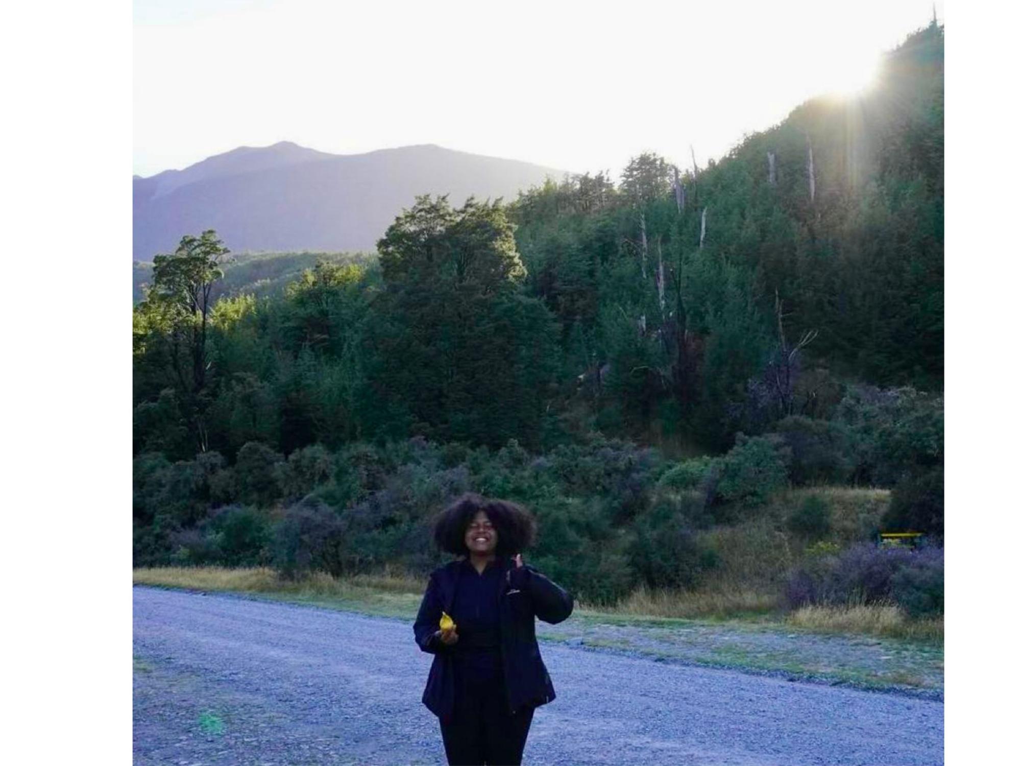 person stands in front of forest with volcano in distant background