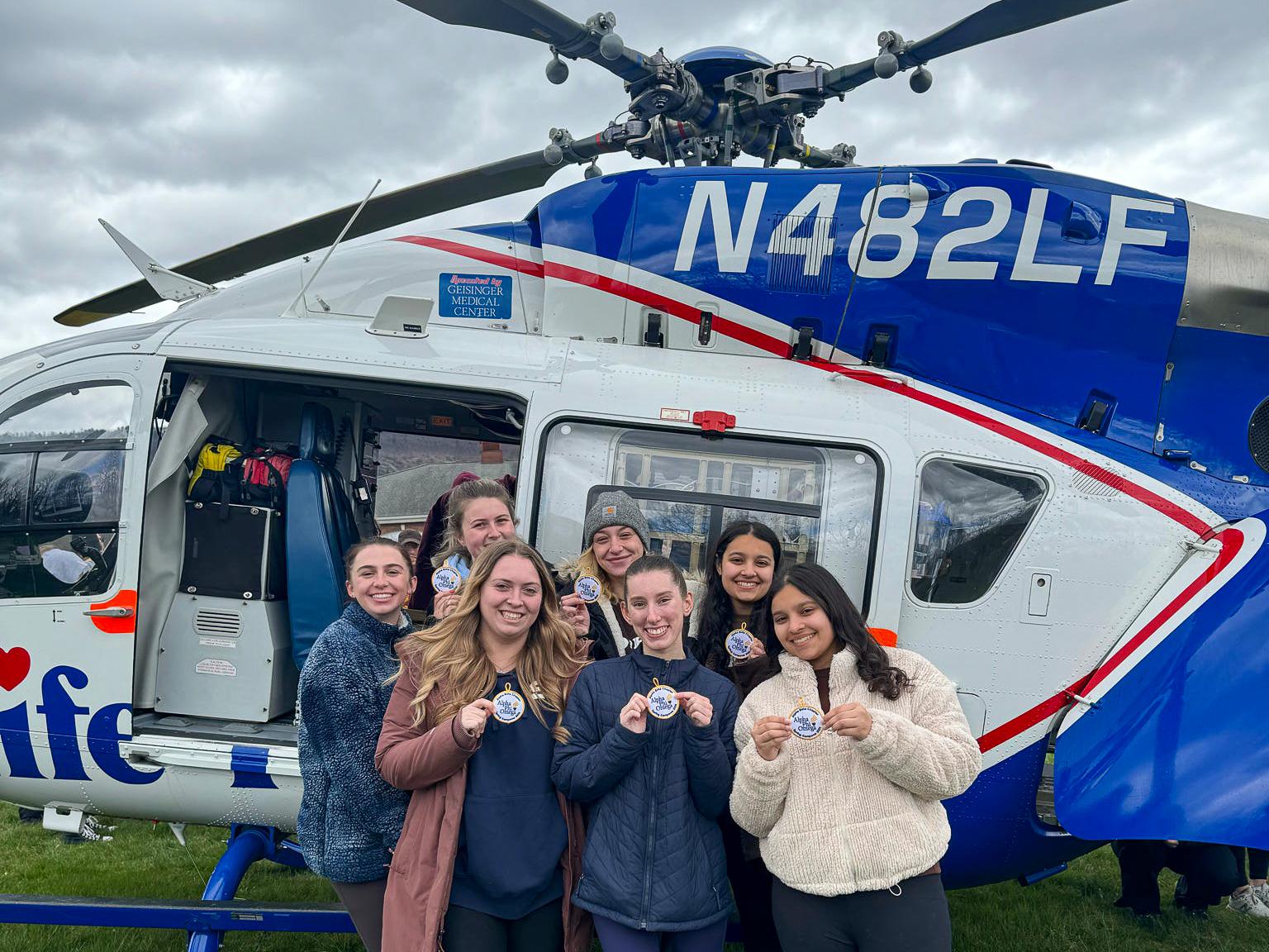 Seven Penn State students stand in front of a helicopter while holding up badges.