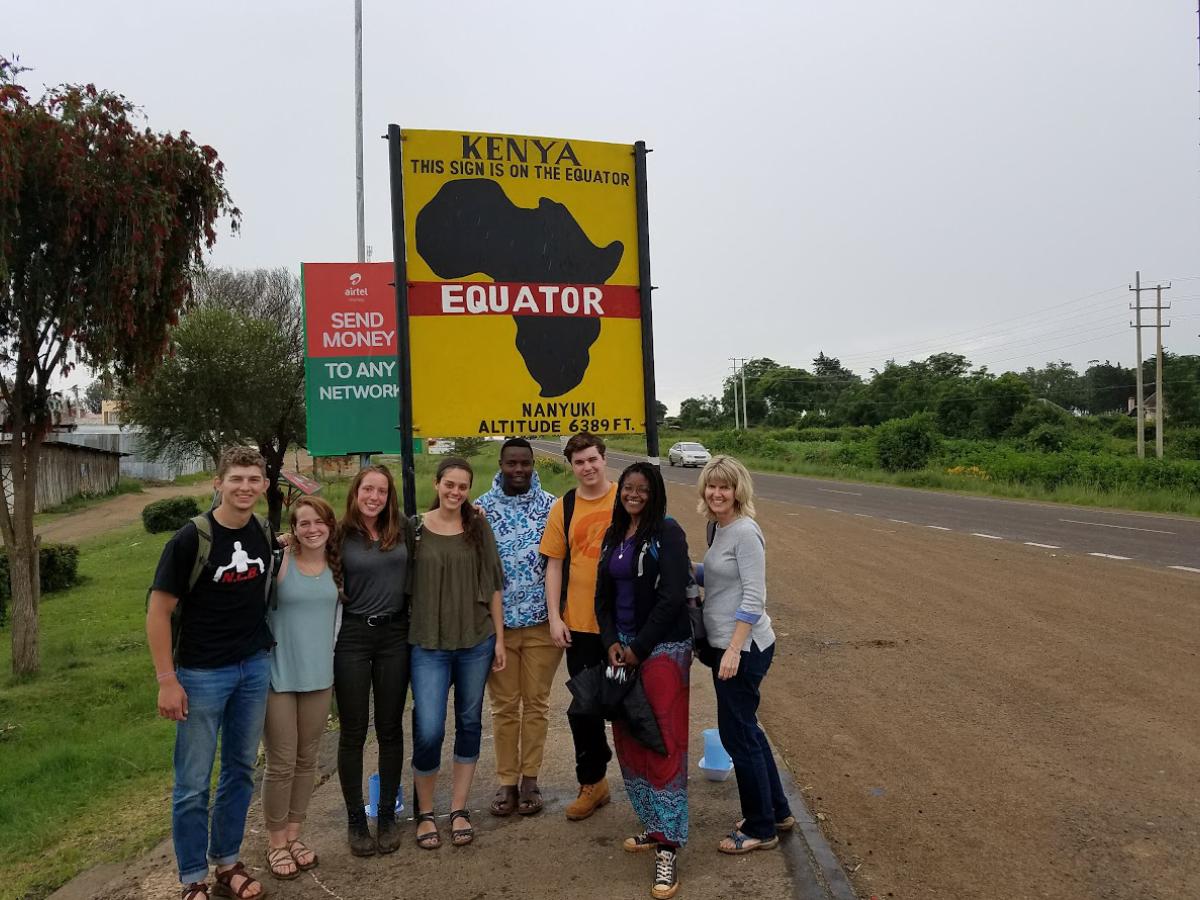 Teacher and students stand in front of a sign marking the equator in Kenya