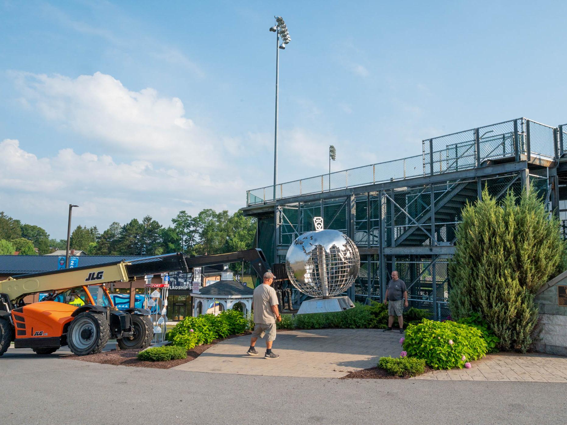 A large stainless steel globe is lowered into place by a crane