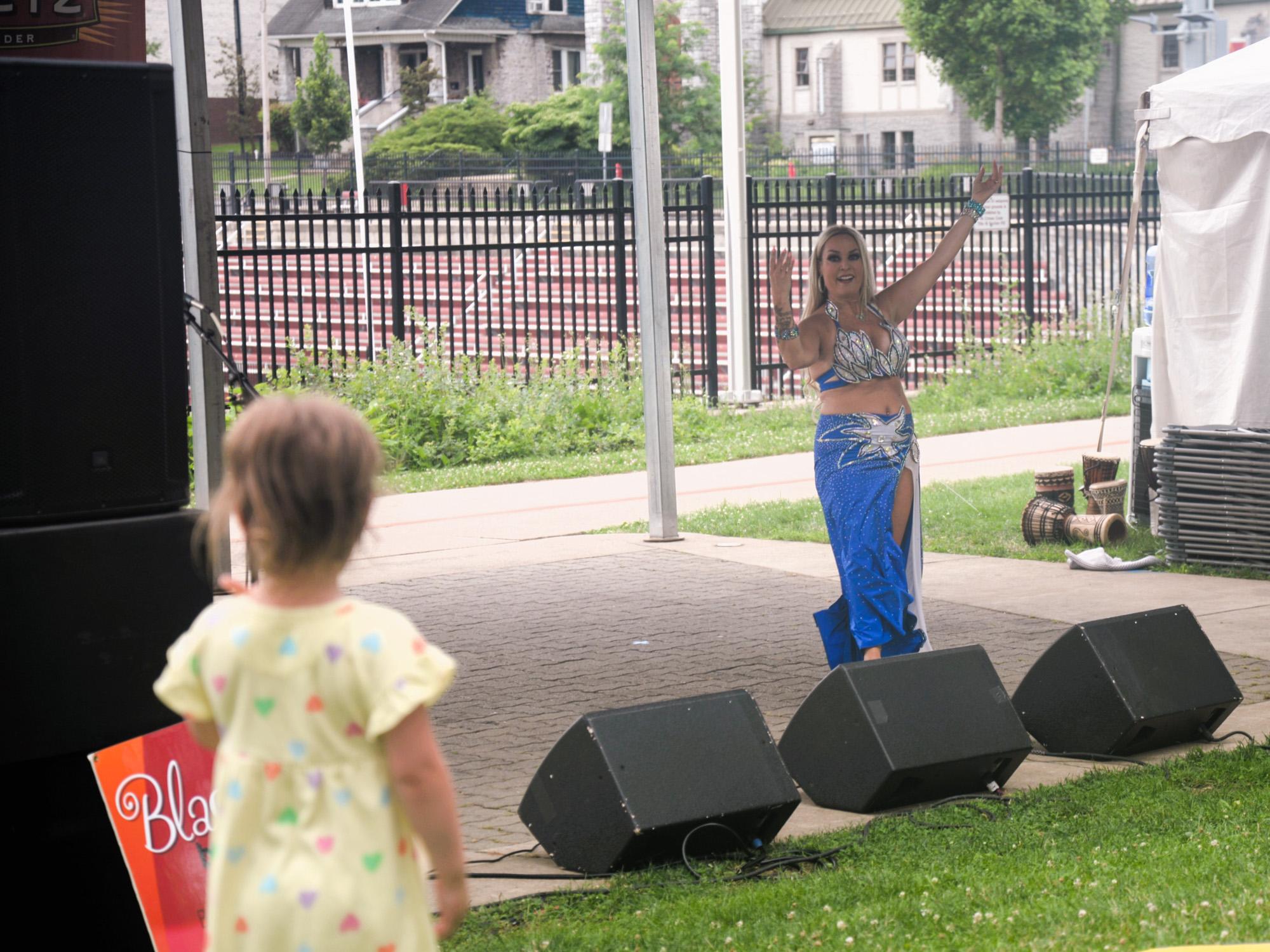 A woman dances in the background as a young girl watches her in the foreground