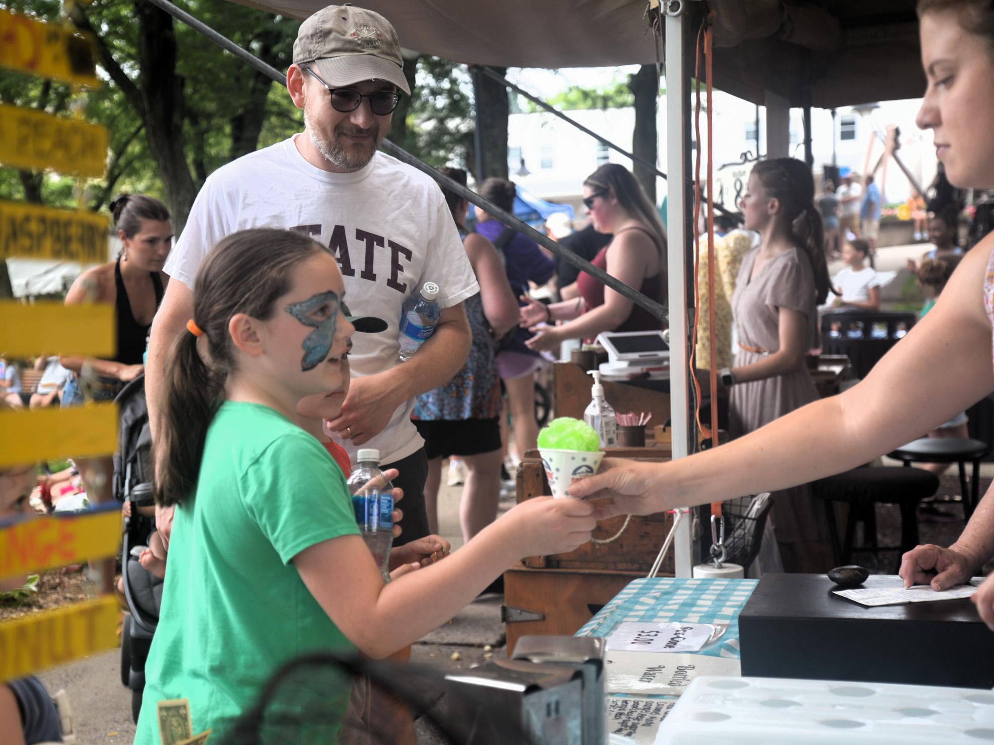 A child accepts a snowcone from a vendor
