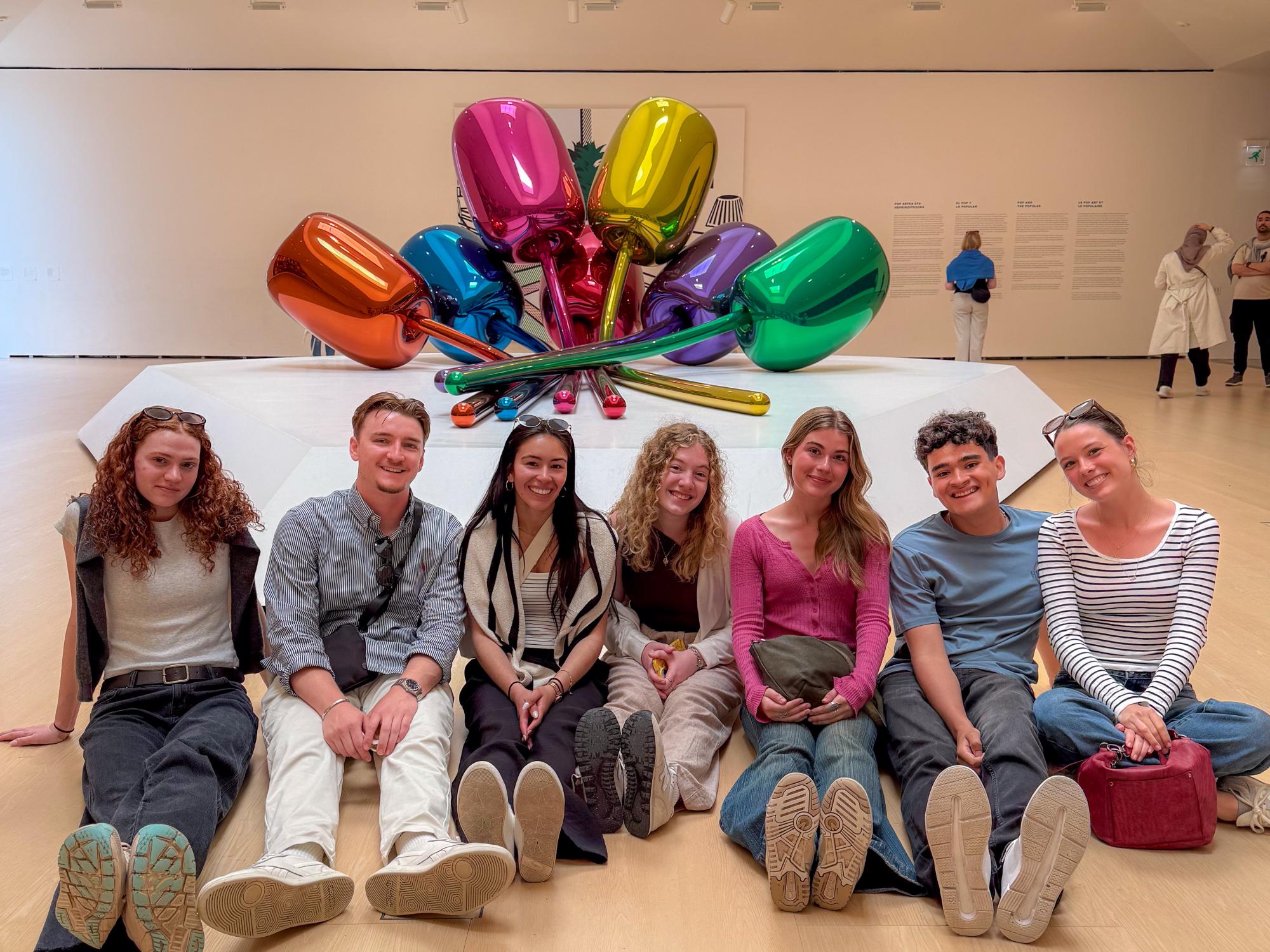 Seven Penn State students sit on the floor of the Guggenheim Museum in front of a modern Jeff Koons sculpture in Bilbao, Spain.