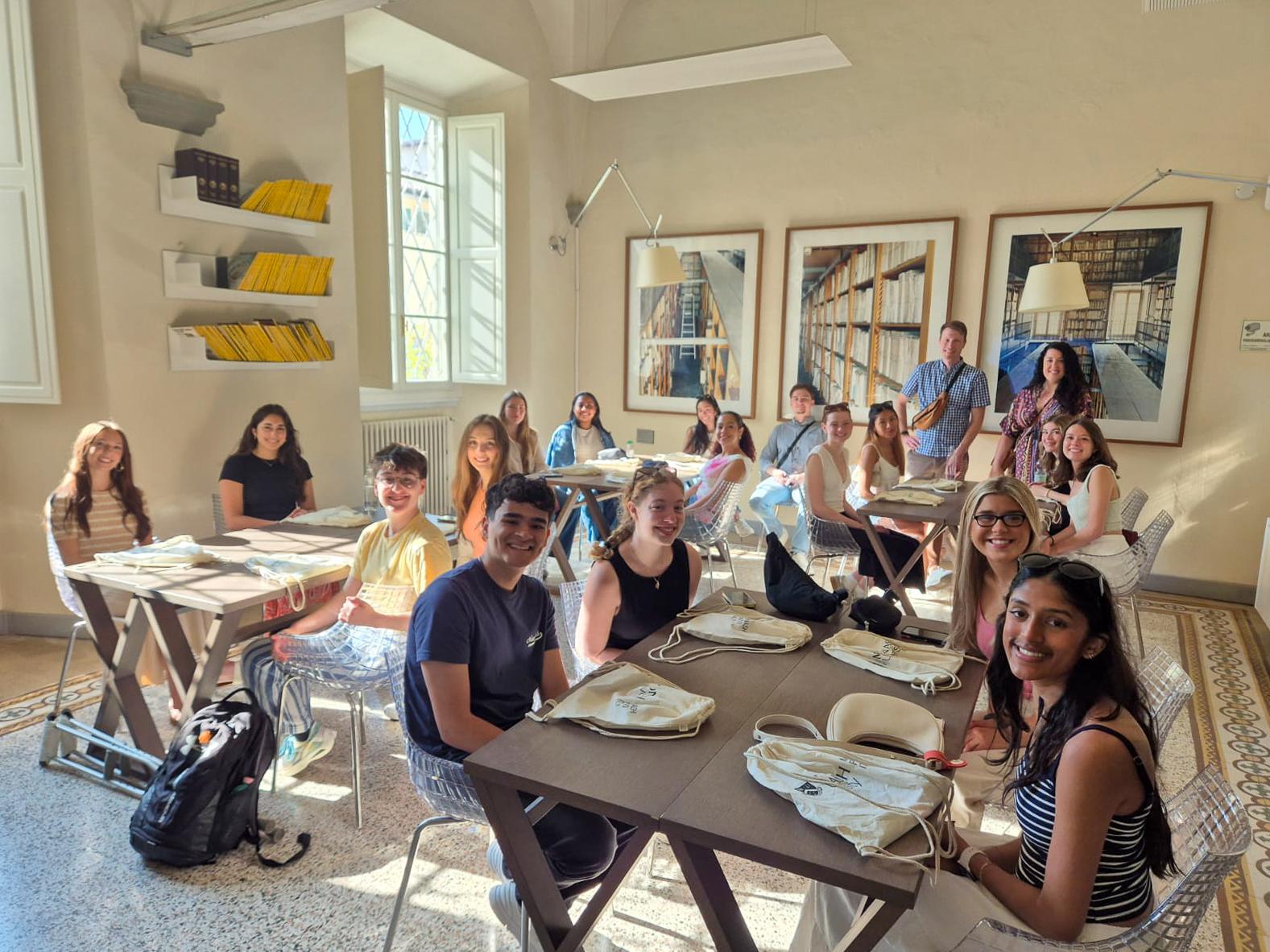 Penn State students sit at tables during orientation in Prato, Italy, while faculty stand behind them.
