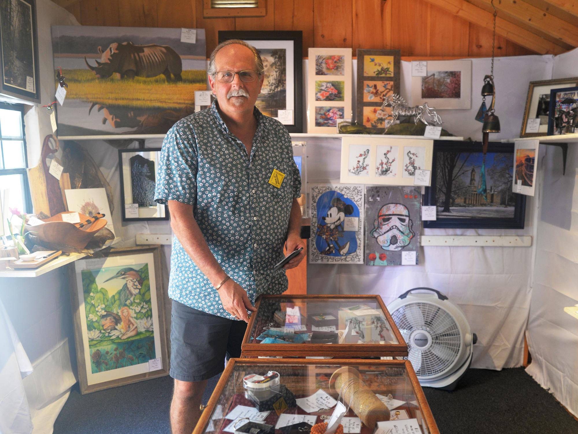 A smiling person stands in a gallery filled with fine arts and crafts
