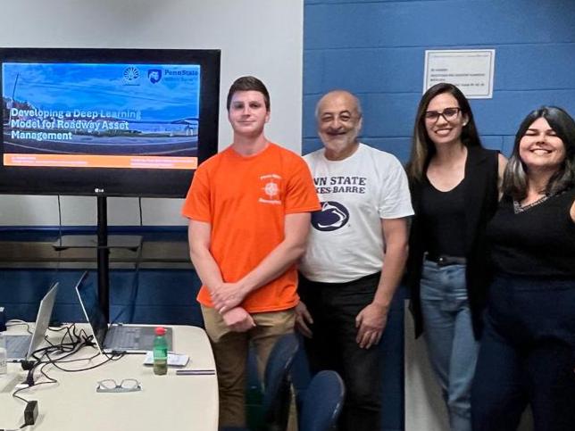 A group of eight people standing against a wall with a computer screen at the center. 