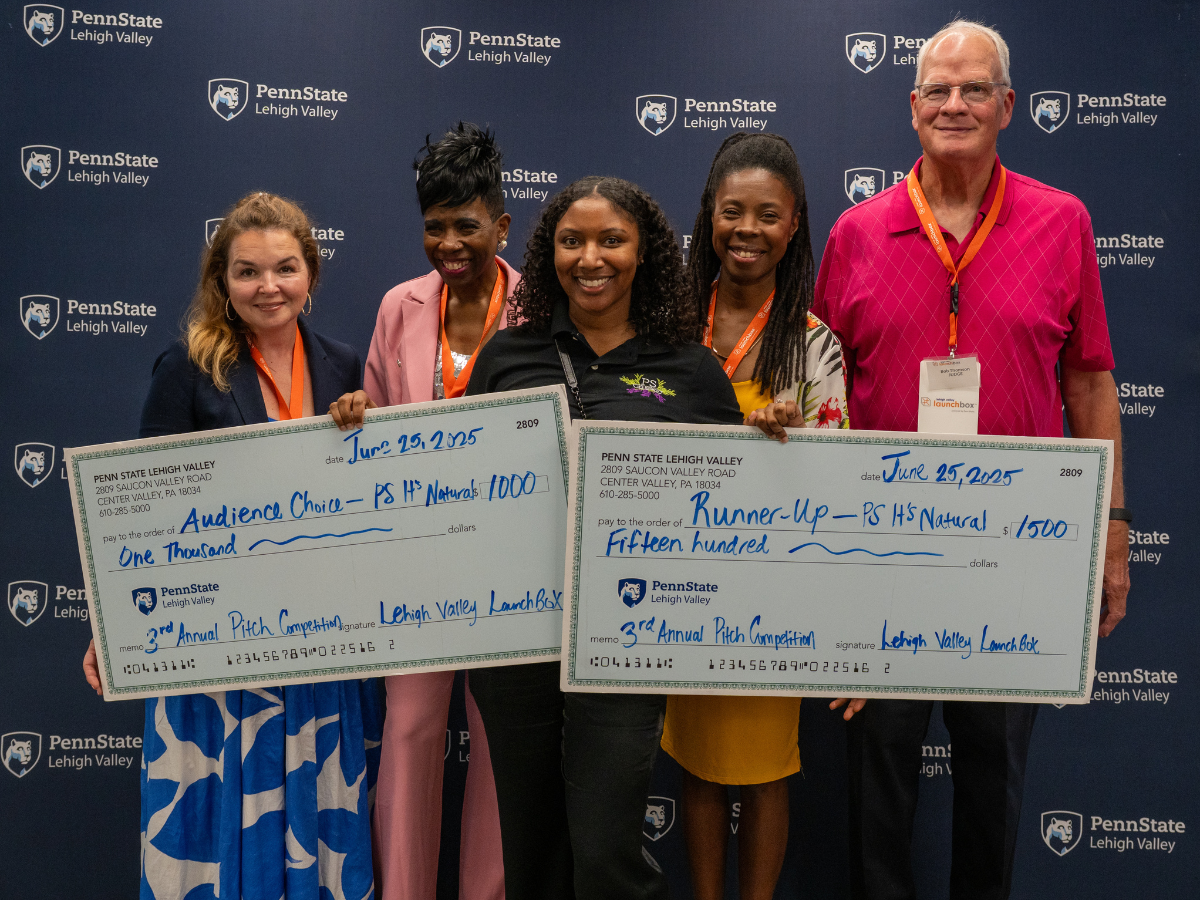 a woman, smiling holds two large checks with people beside her 