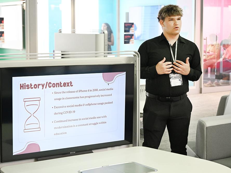 A student stands next to a monitor while giving a presentation.