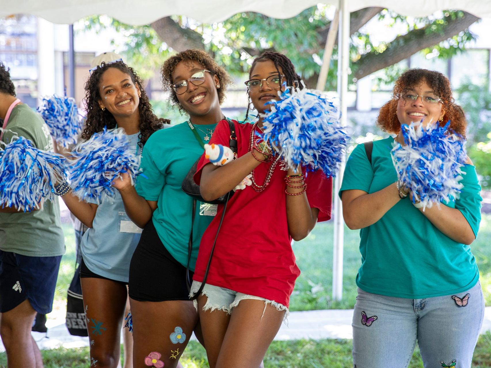 Four students holding blue and white pom poms smile for the camera