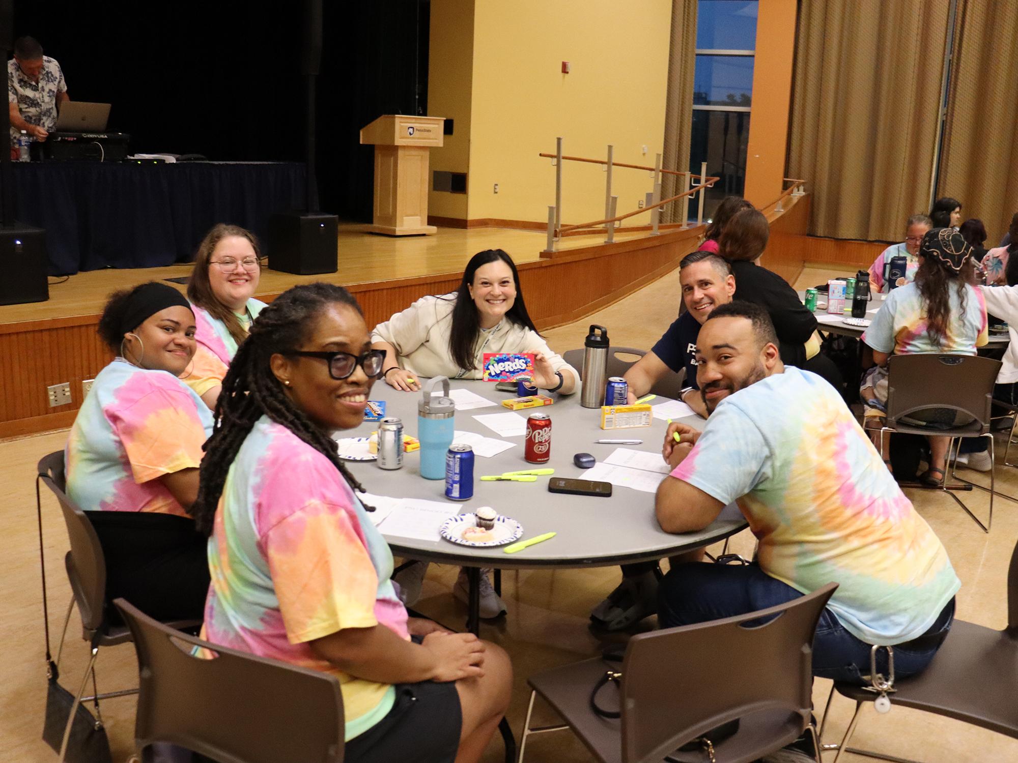 People wearing tie-dye T-shirts sit at a table in a large room.