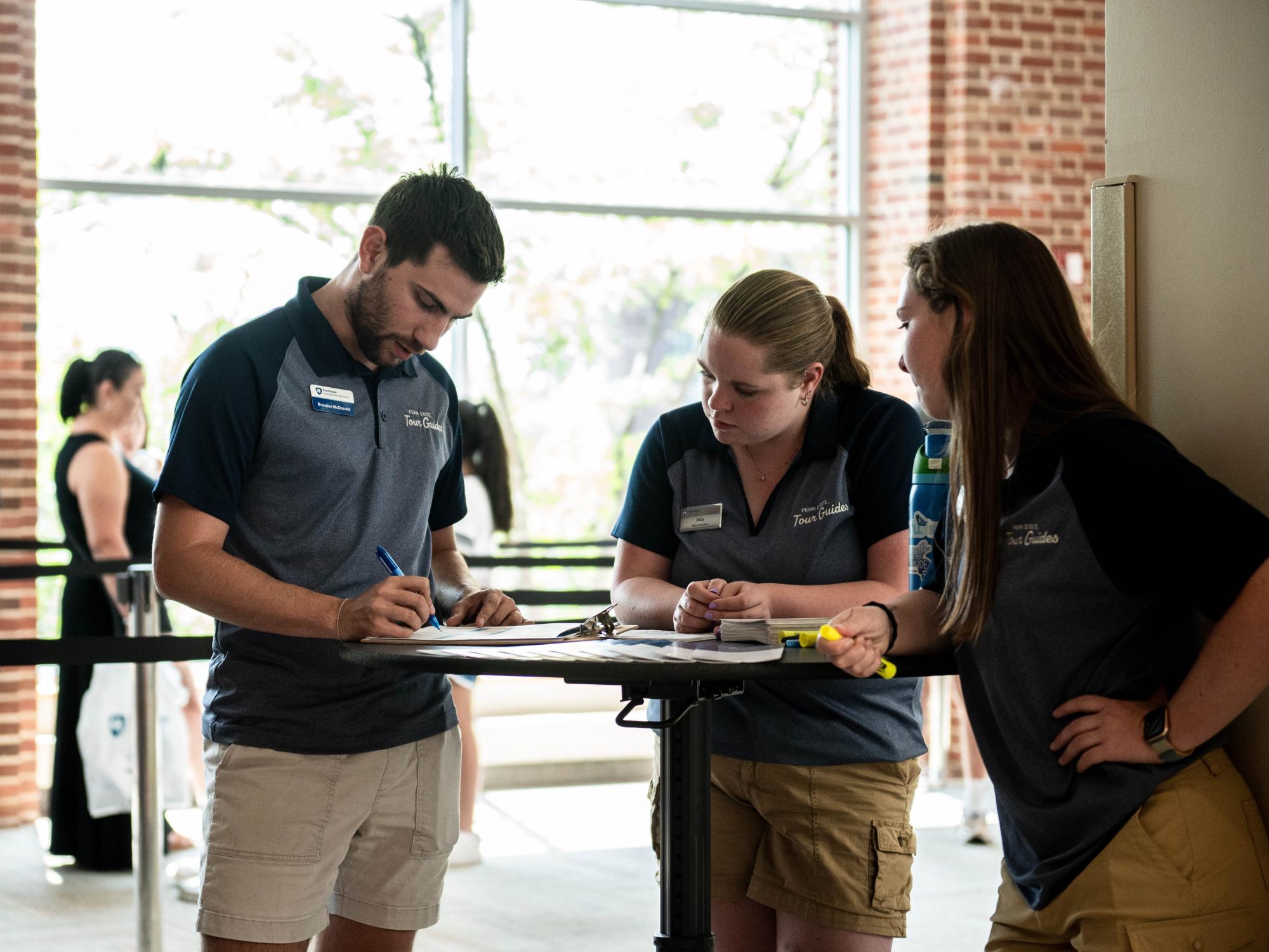 Three individuals stand at a table and look at materials on the table