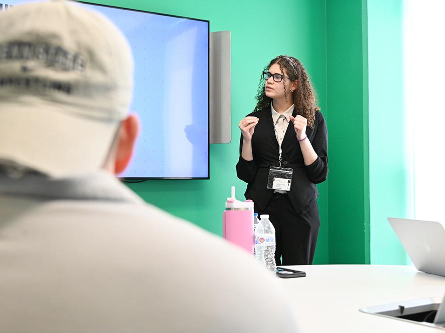 A student stands next to a monitor while giving a presentation.