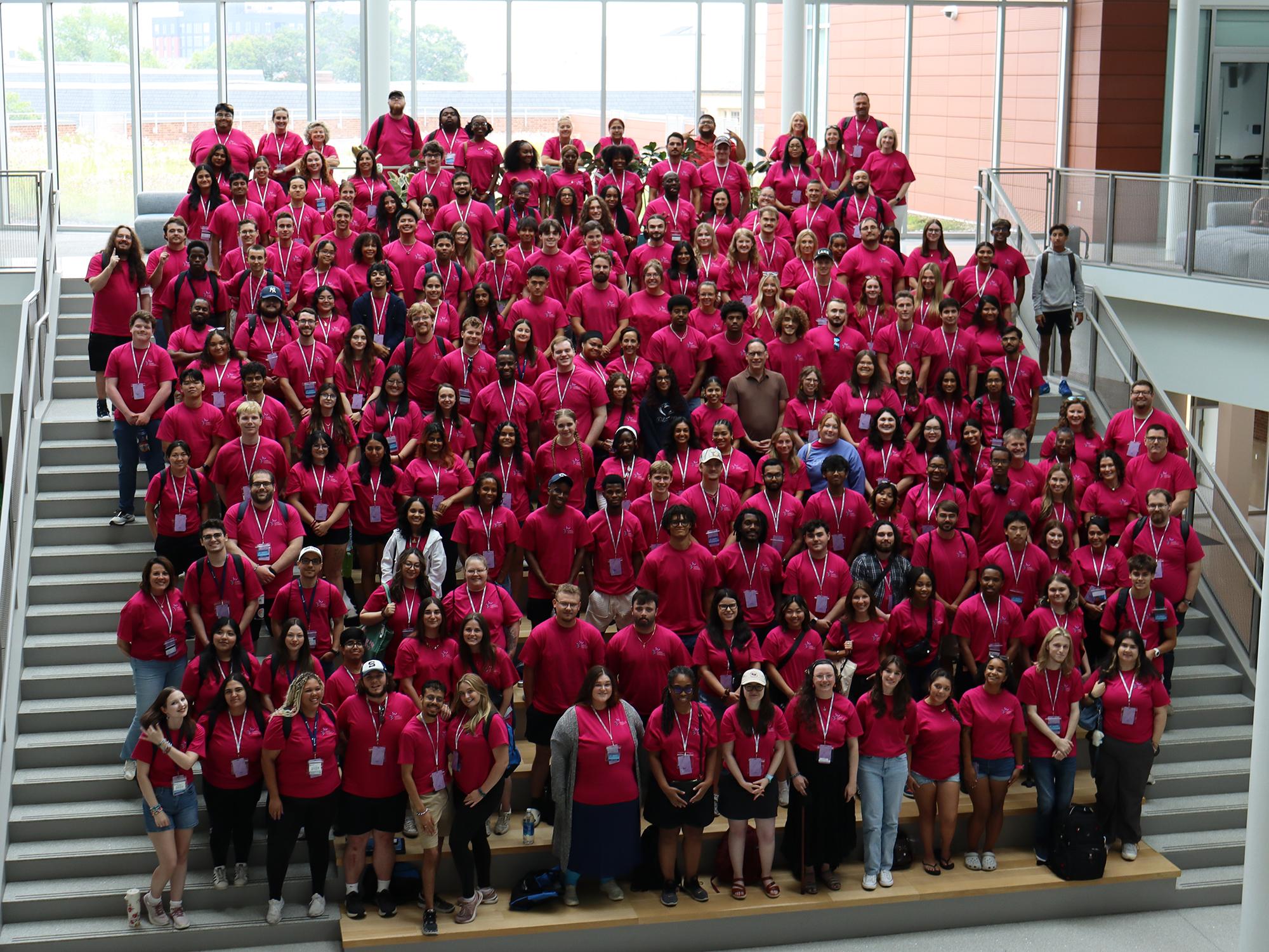 A large group of people wearing red shirts pose on a large set of indoor stairs.