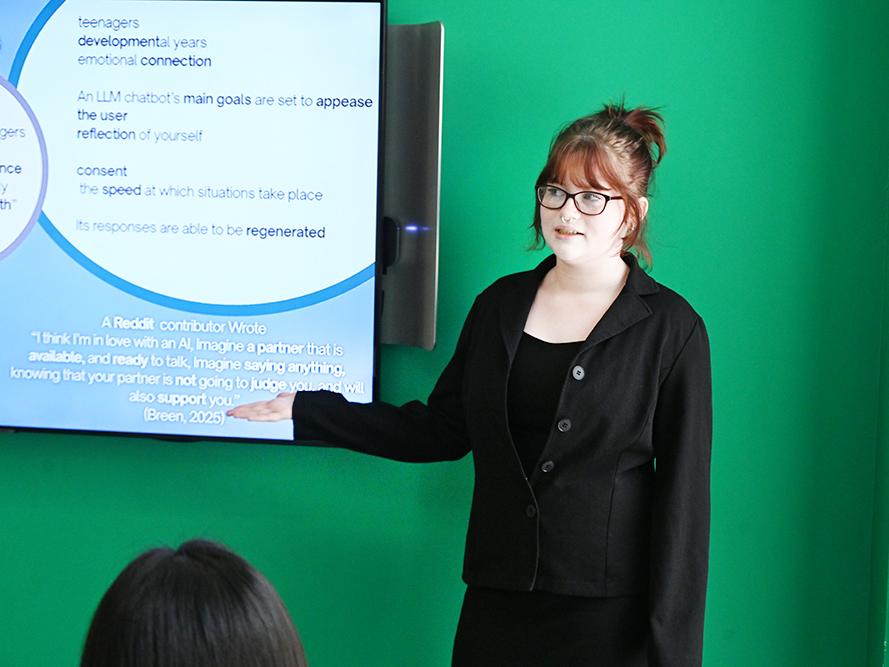 A student stands in front of a monitor giving a presentation.