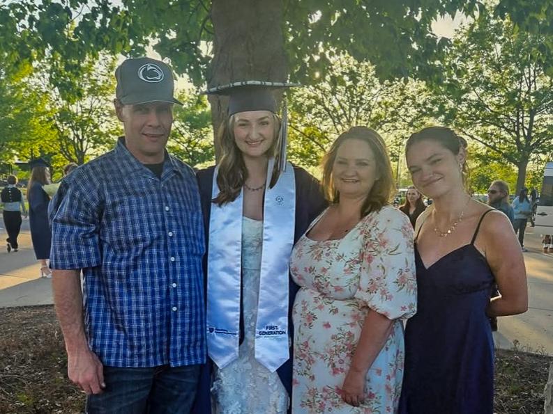 Cwalina wears her graduation gown and stands with her family members at commencement.