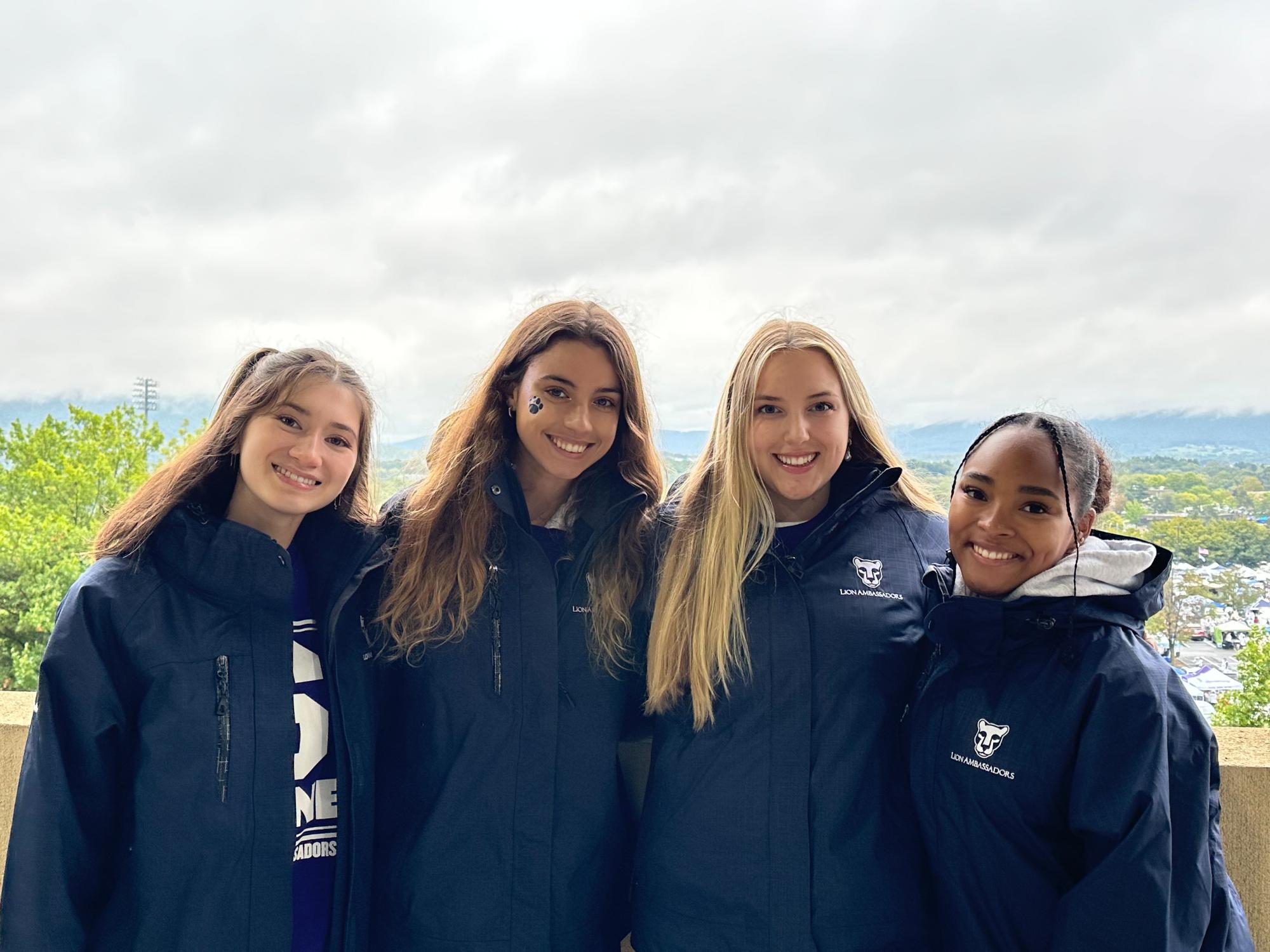 Emma Suzuki Szwajkowski (left) and her fellow Lion Ambassadors stand against a wall in Beaver Stadium with a view of parking lots behind them.