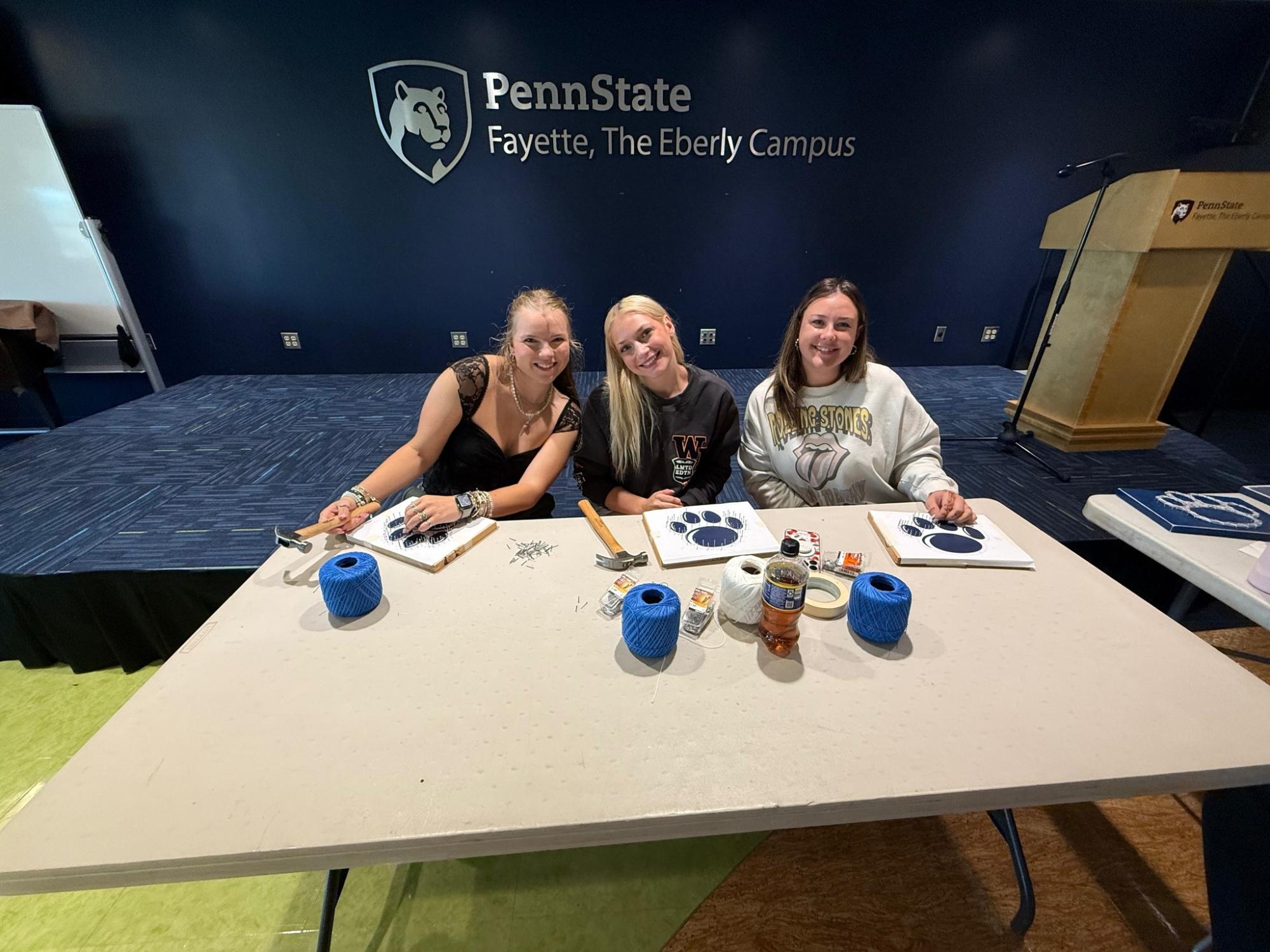Three students smile for the camera while working on an art project