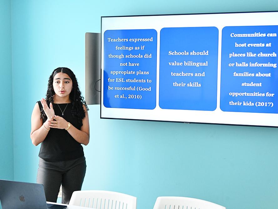 A student stands next to a monitor while giving a presentation.