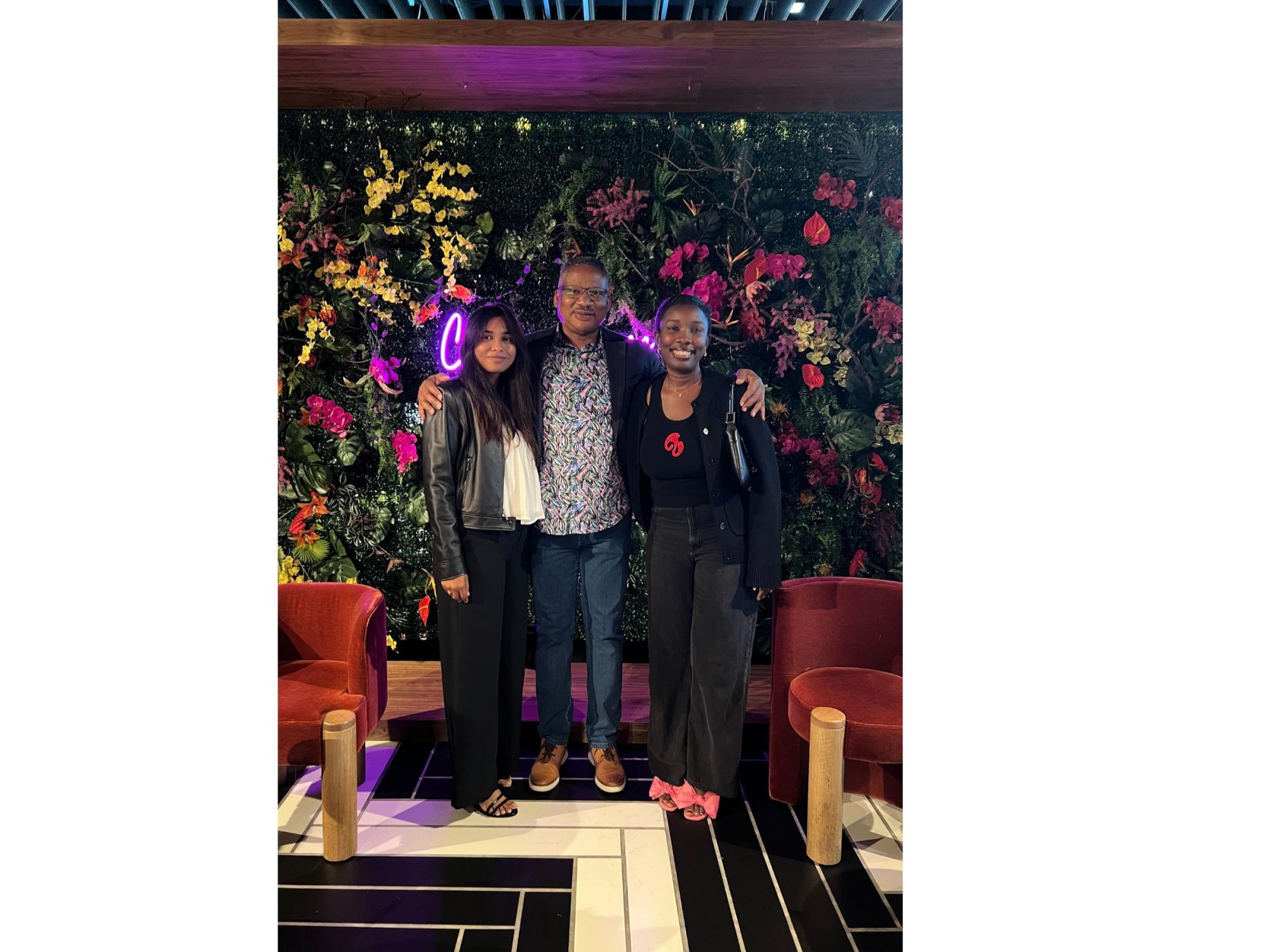 three people stand in front of flower wall