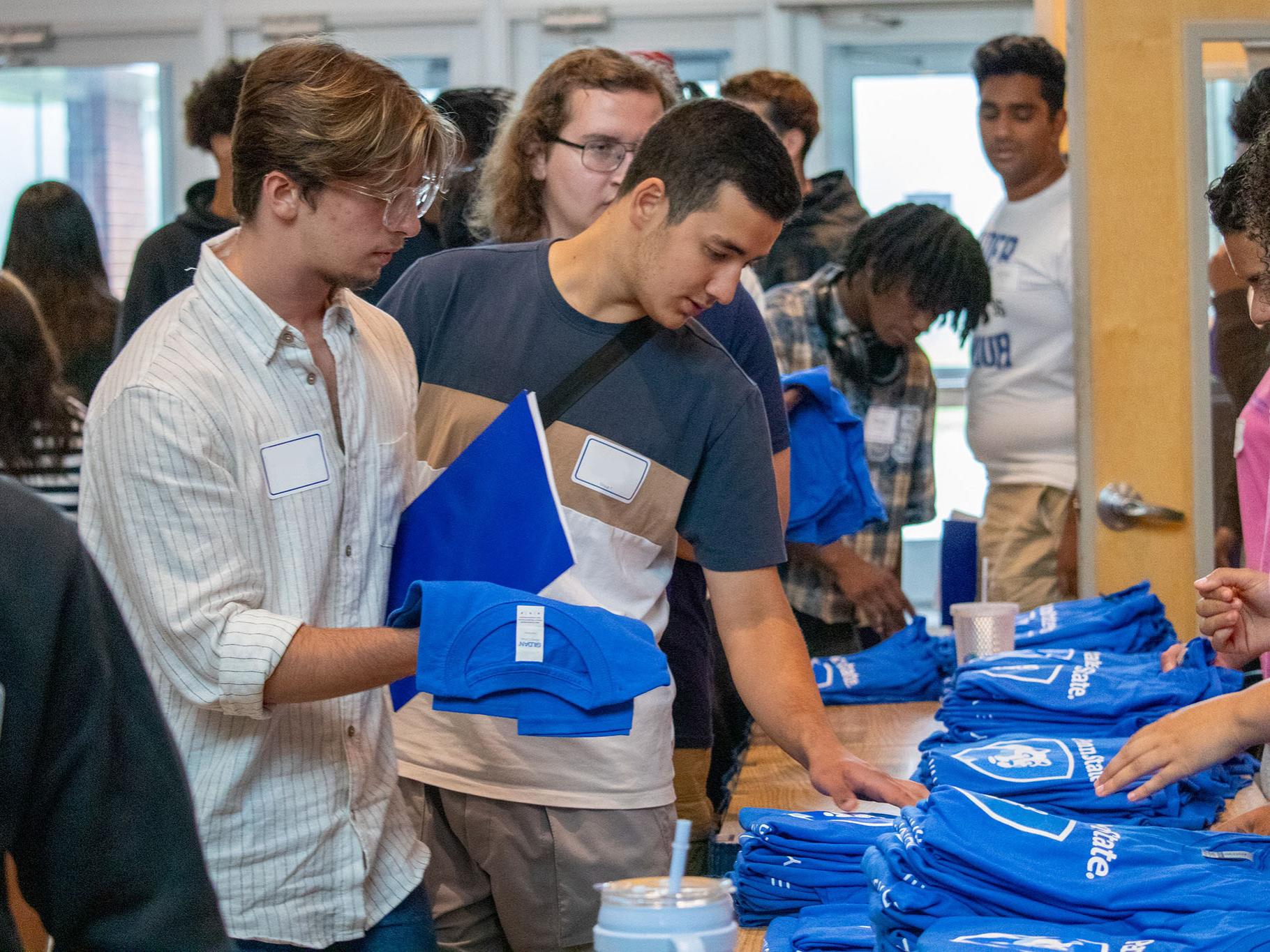 Two students look at t-shirts folded on a table