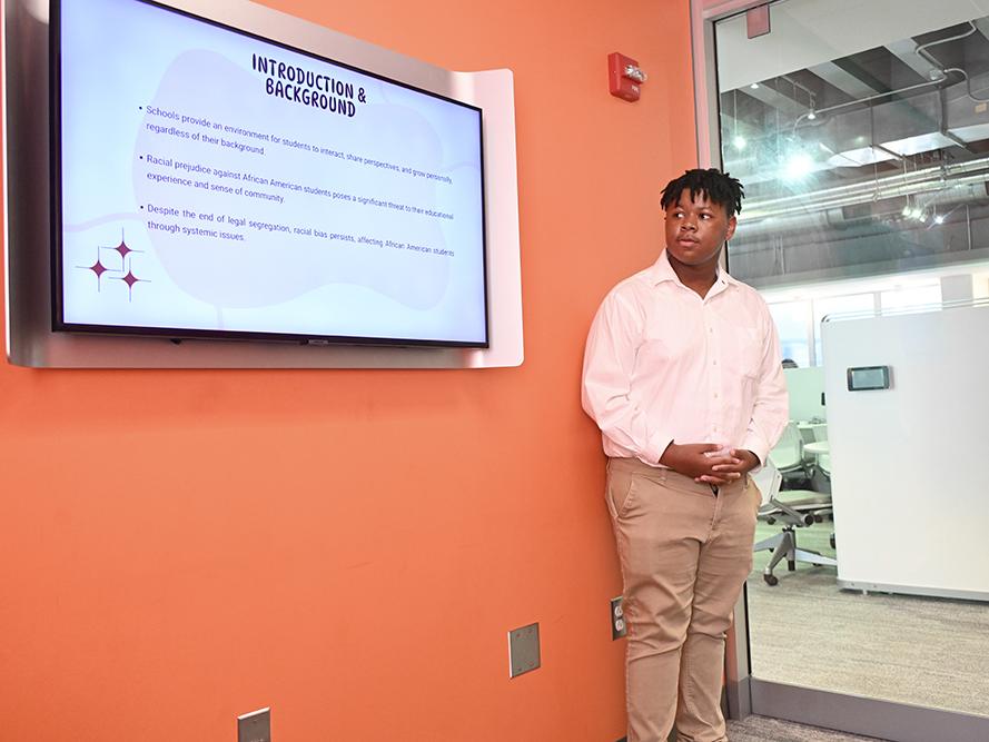 A student stands next to a monitor while giving a presentation.