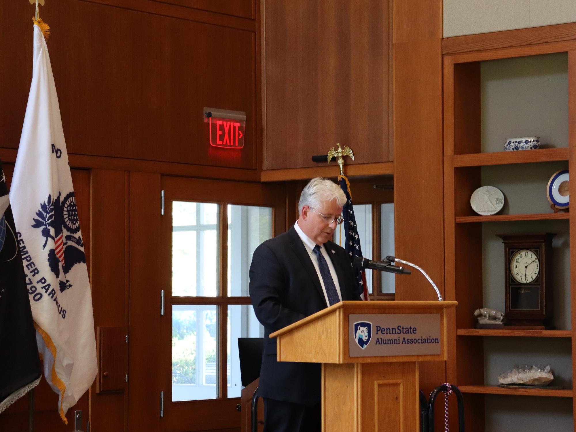 A man speaks at a podium in front of a group of flags.