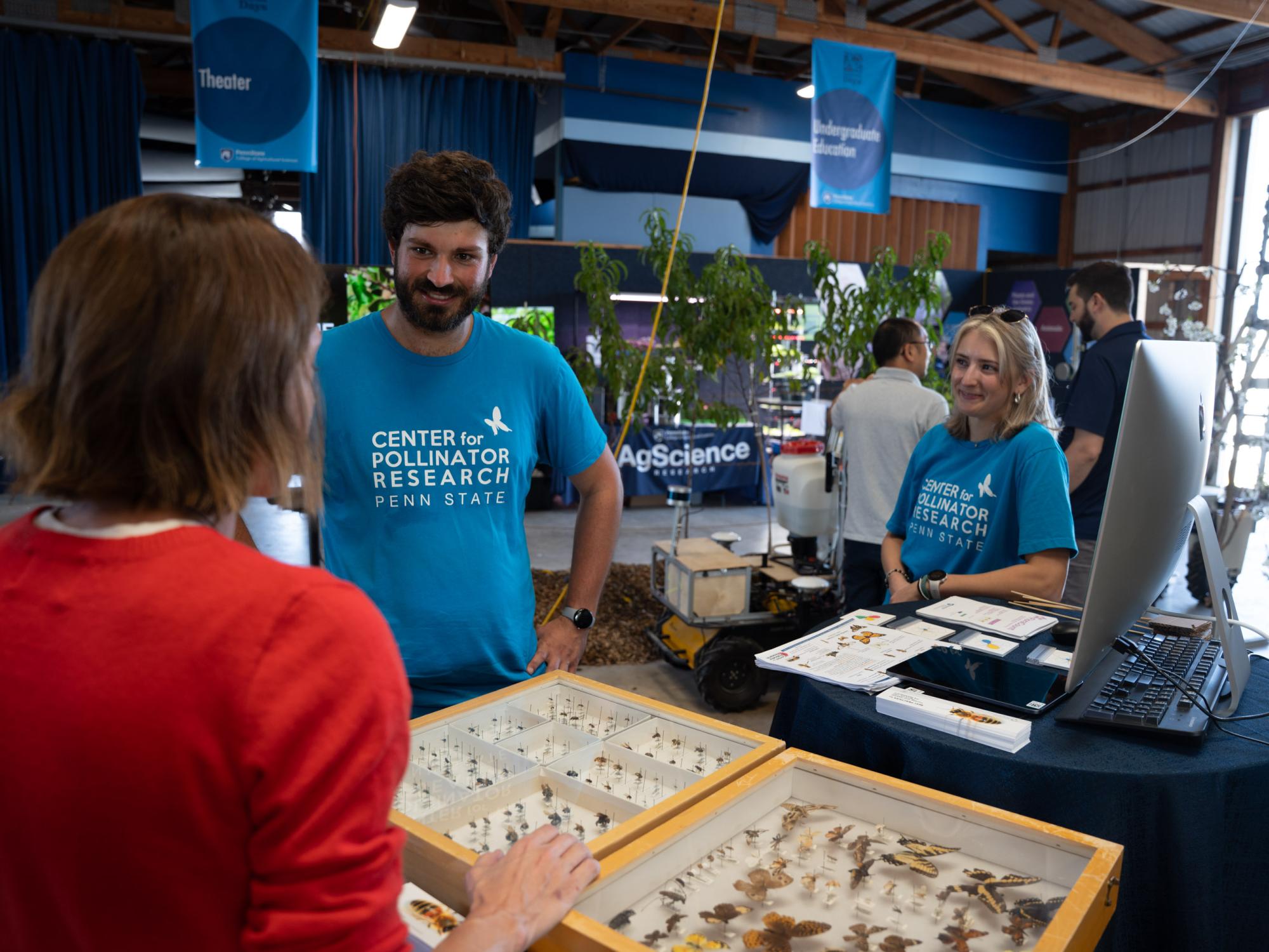 Two educators show a fair visitor an exhibit on pollinators